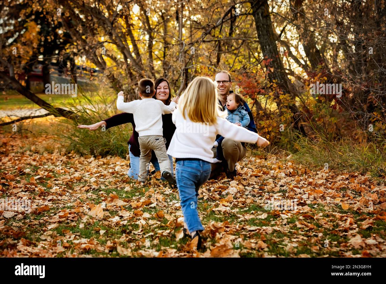 Junge Familie mit drei Kindern, jüngste Tochter mit Down-Syndrom, die in der Herbstsaison gemeinsam in einem Stadtpark Spaß hat Stockfoto