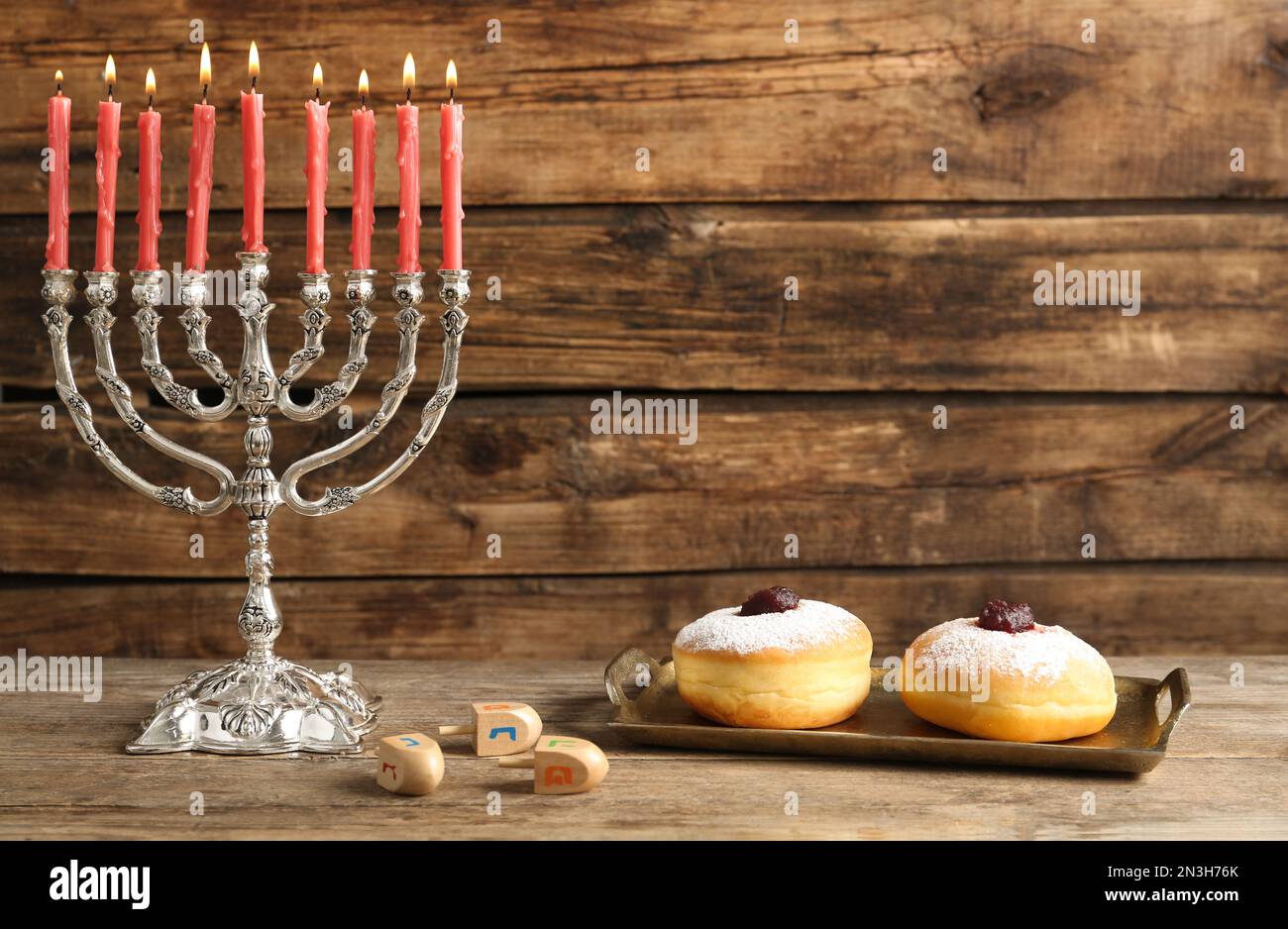 Silberne Menora in der Nähe von Sufganiyot und Dreidel mit den Symbolen Nun, He, PE, Gimel auf Holzhintergrund, Platz für Text Stockfoto