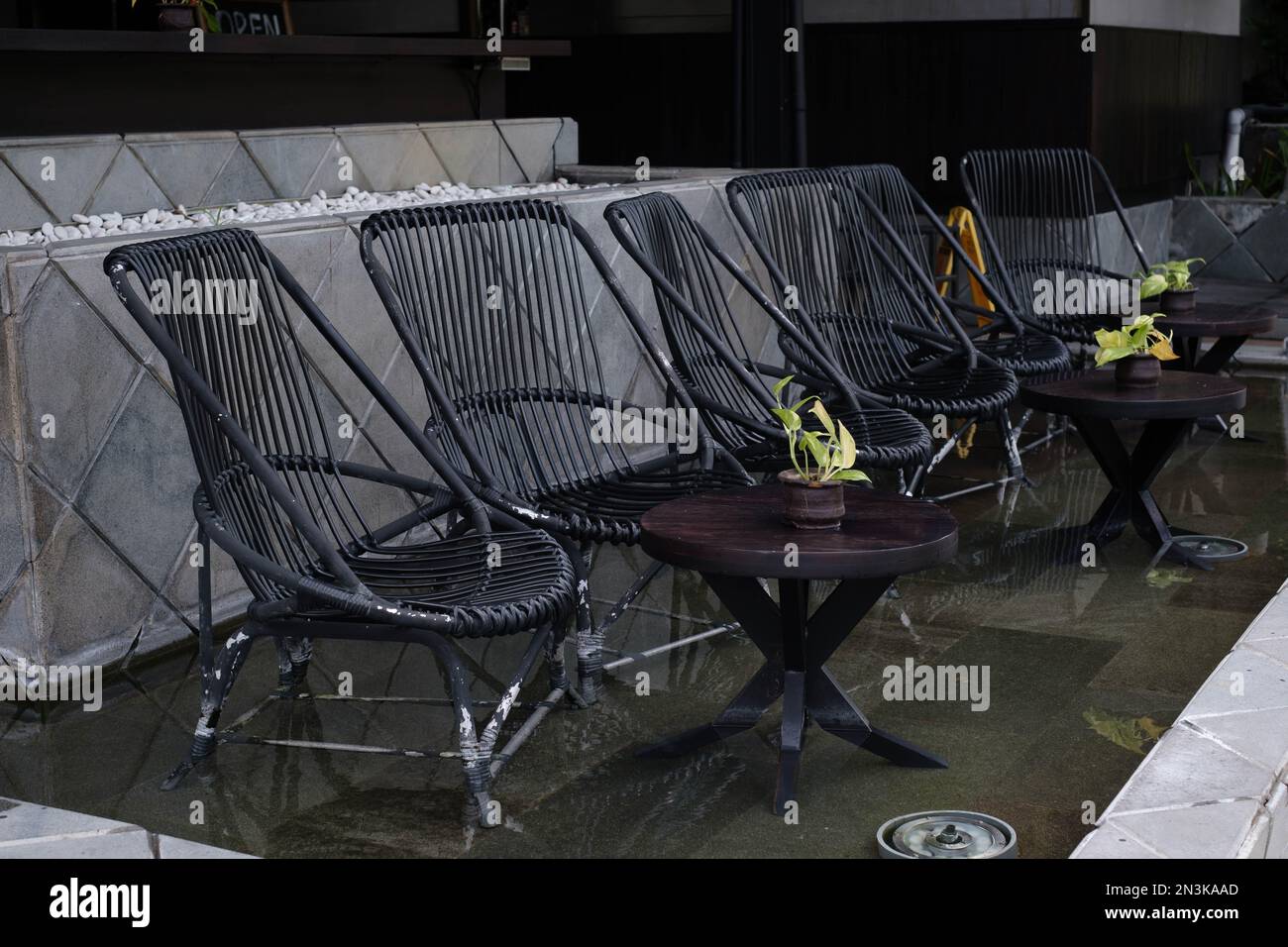 Atemberaubende Außenumgebung mit schwarzem Basaltteich mit modernen schwarzen Stühlen und Tischen, die sich auf der Oberfläche spiegeln Stockfoto