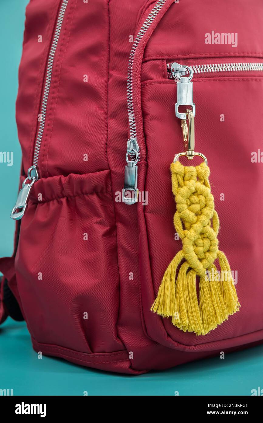 Nahaufnahme des handgefertigten Macrame-Schlüssels, der auf dem roten Rucksack hängt, isoliert auf dem tiffany-blauen Hintergrund. Stockfoto
