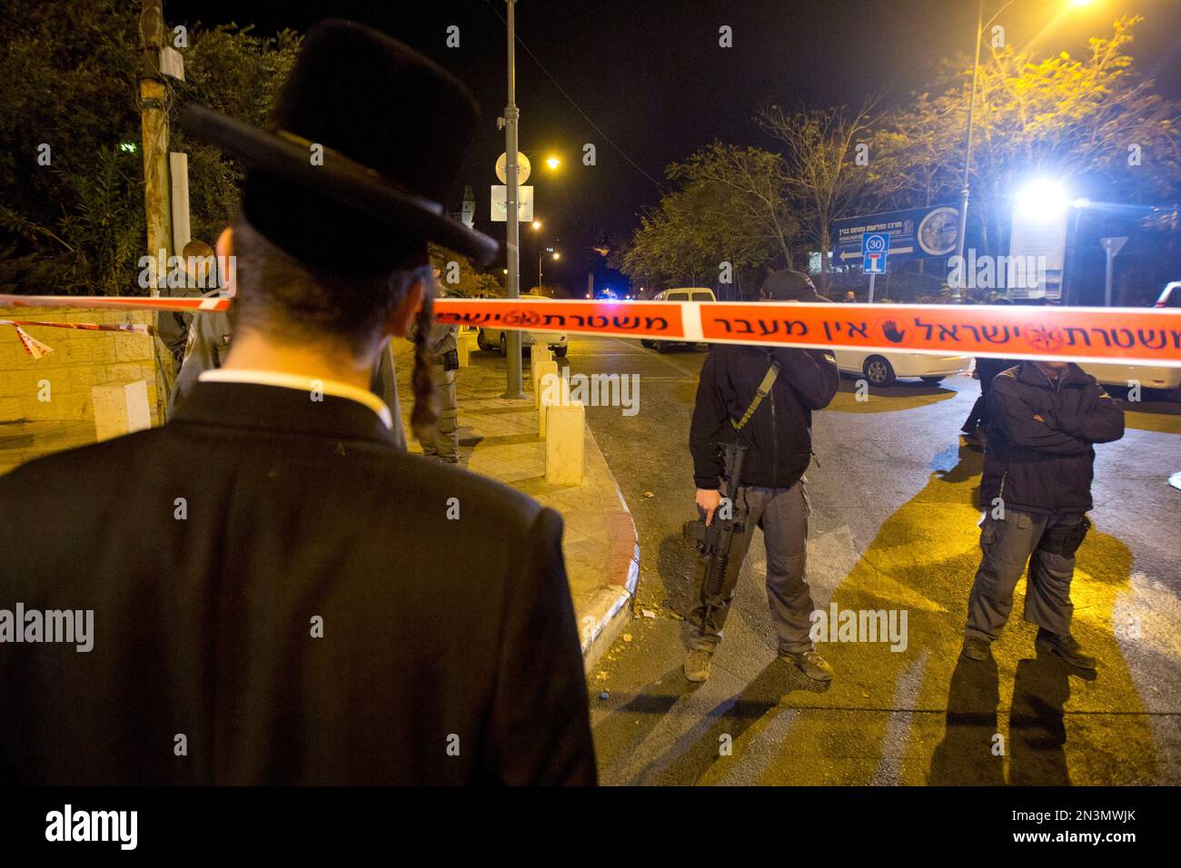 FILE - In this Wednesday, Oct. 29, 2014 file photo, an ultra-Orthodox Jewish man looks as Israeli police officers stand guard at the scene of a shooting in Jerusalem. This combustible city at the center of the Israeli-Palestinian conflict has been edging toward a new conflagration, with politicians on both sides stoking religious fervor over an ancient shrine, known to Muslims as the Noble Sanctuary and to Jews as the Temple Mount, that is sacred to both. (AP Photo/Sebastian Scheiner, File) Stockfoto