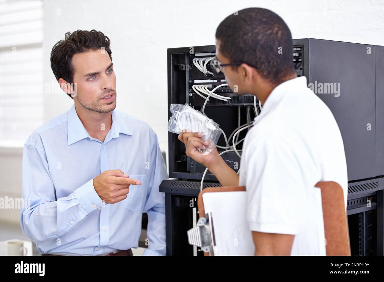 Das ist nicht das Kabel, um das ich gebeten habe. Ein Mann hält ein Kabel für den Computer und hat Streit mit einem anderen Geschäftsmann. Stockfoto