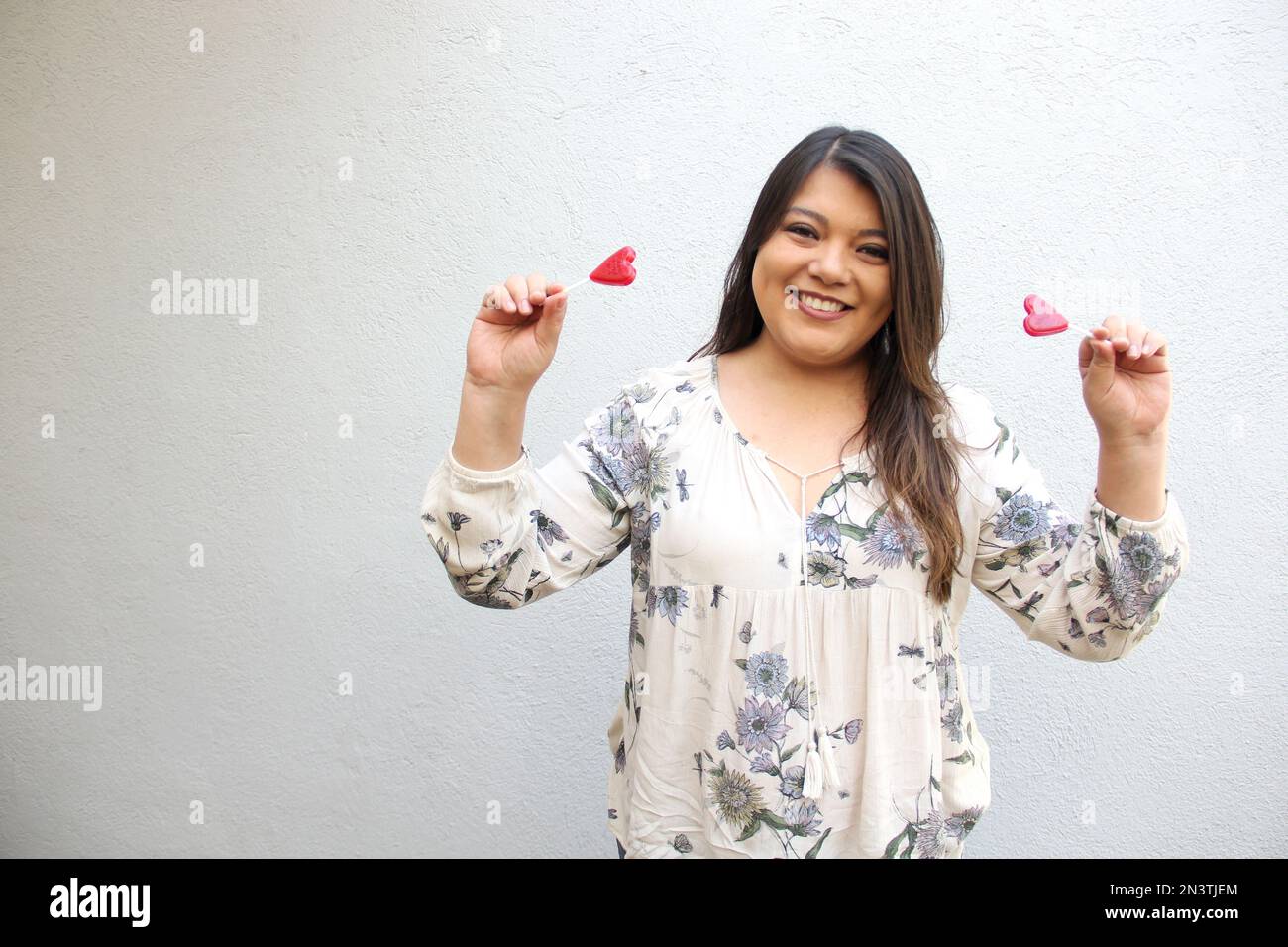 Lateinische Erwachsene Frau mit roten herzförmigen Lutschern, um ihre Begeisterung für die Ankunft im Februar zu zeigen und ihre Zuneigung zum Valentinstag zu feiern und zu zeigen Stockfoto