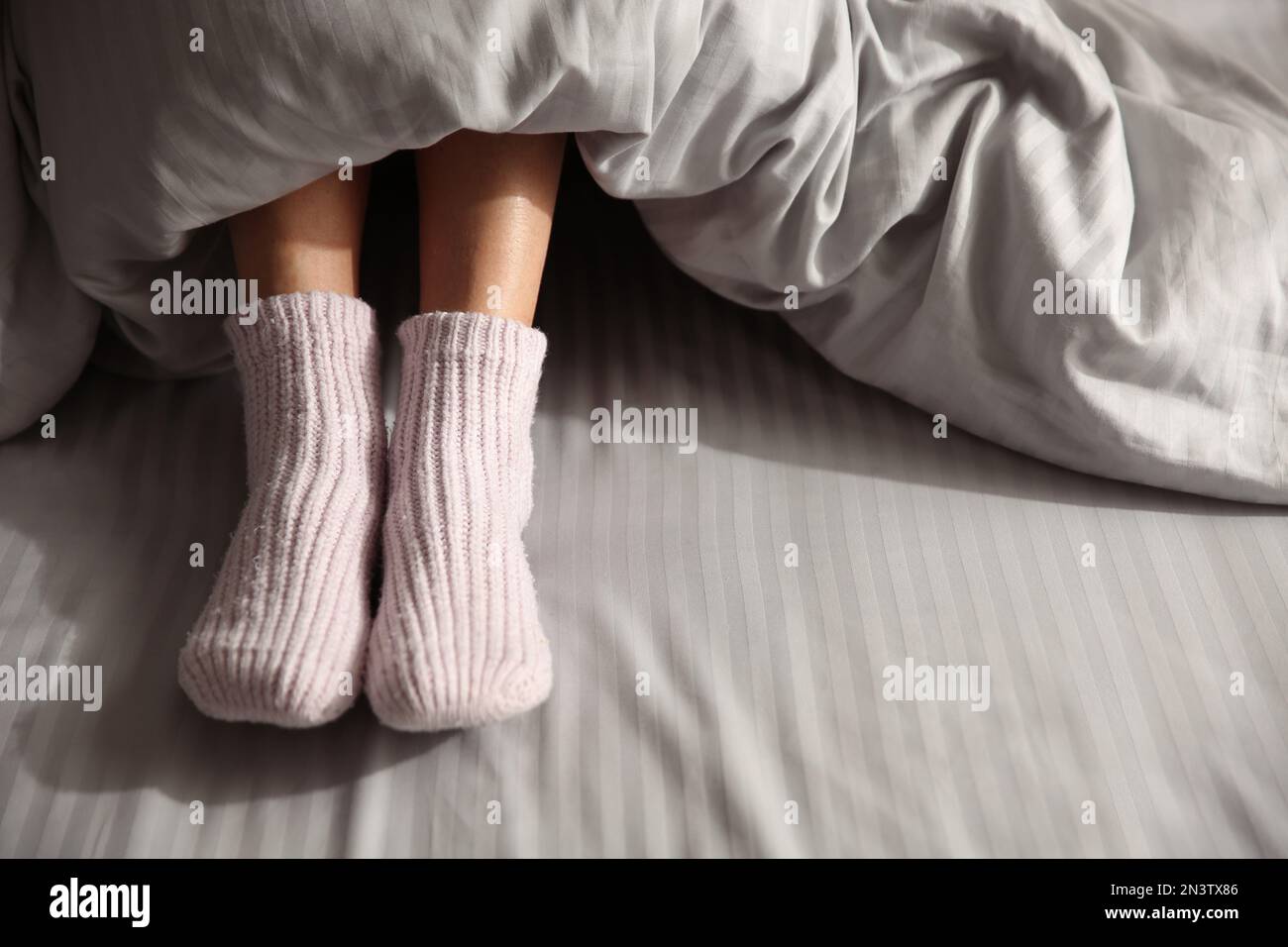 Eine Frau trägt gestrickte Socken unter einer Decke im Bett, Nahaufnahme Stockfoto