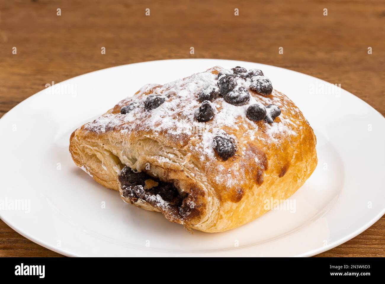 Dänische Pastete gefüllt mit Schokoladencreme mit Schokoladenchips und Puderzucker in weißer Keramikschale auf Holztisch mit Schneideweg Stockfoto