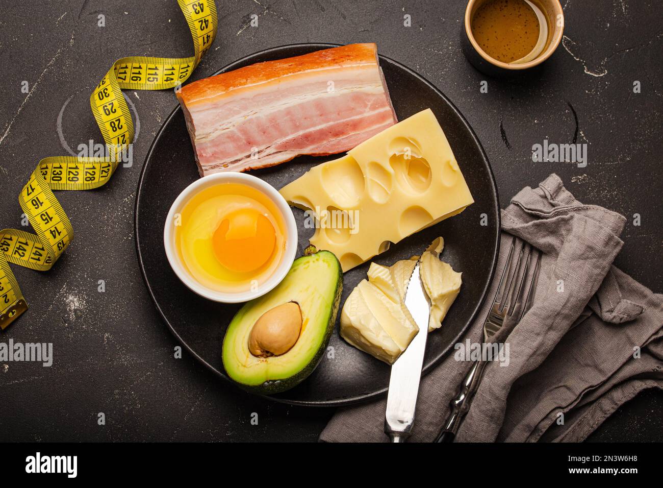 Keto-Lebensmittel wie Butter, Olivenöl, Spiegelei, Avocado, fettartiger Speck, Käse für ketogene Ernährung auf schwarzer Platte, Band auf dunklem rustikalem Stein abmessen Stockfoto