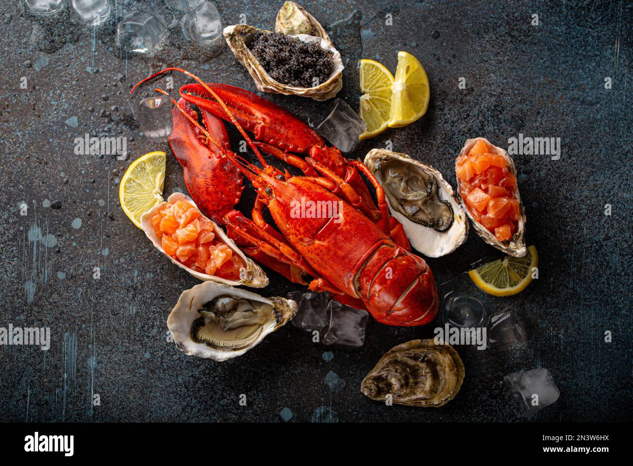 Gemischter Fisch- und Meeresfrüchteteller mit gekochtem roten Hummer, frischen offenen Austern, schwarzem Kaviar, Lachs-Tartare, serviert mit Zitronenspalten und Eiswürfeln Stockfoto