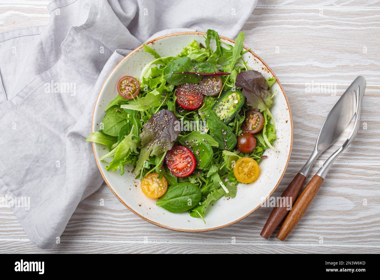 Gemüse, vegetarischer gesunder Salat mit roten gelben Kirschtomaten, grünen Blättern und Chiasamen auf weißem Teller auf weißem Holz, rustikalem Hintergrund Stockfoto