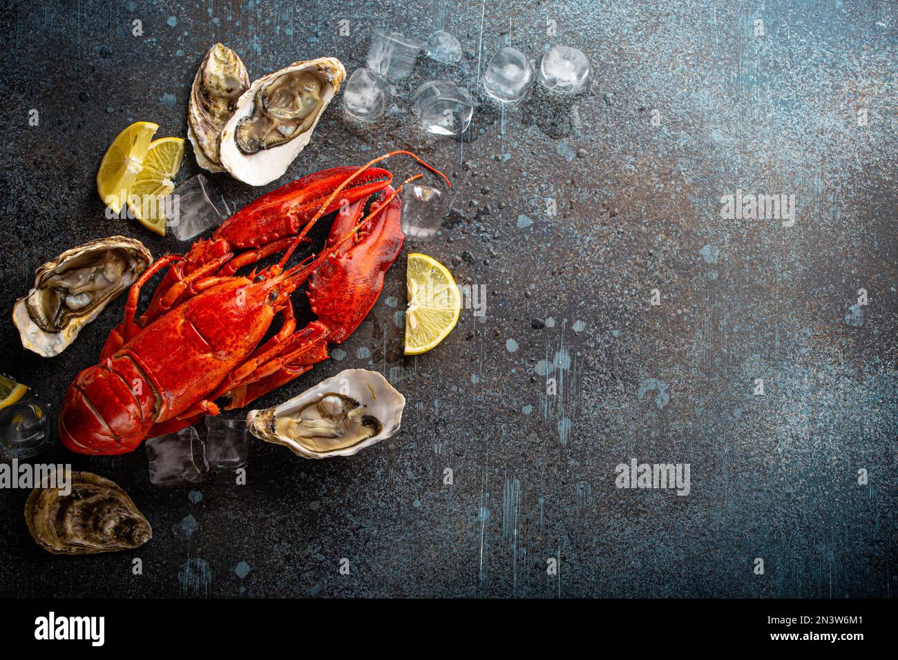 Gekochter, roter Hummer, fertig zum Essen, und frische, offene Austern serviert mit Zitronenschnitten und Eiswürfeln, Blick von oben flach auf blauem Betonstein Stockfoto