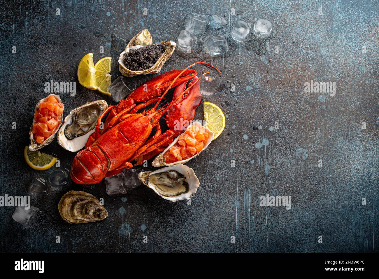 Gemischter Fisch- und Meeresfrüchteteller mit gekochtem roten Hummer, frischen offenen Austern, schwarzem Kaviar, Lachs-Tartare mit Zitronenspalten und Eiswürfeln, Blick von oben flach Stockfoto