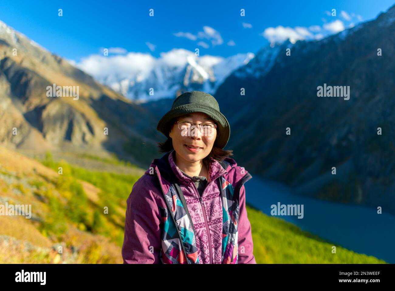 Porträt eines positiven asiatischen Reisenden Mädchens mit Hut und Brille auf dem Hintergrund einer Schlucht mit einem hohen Bergsee Shavlinskoye im Schatten Stockfoto
