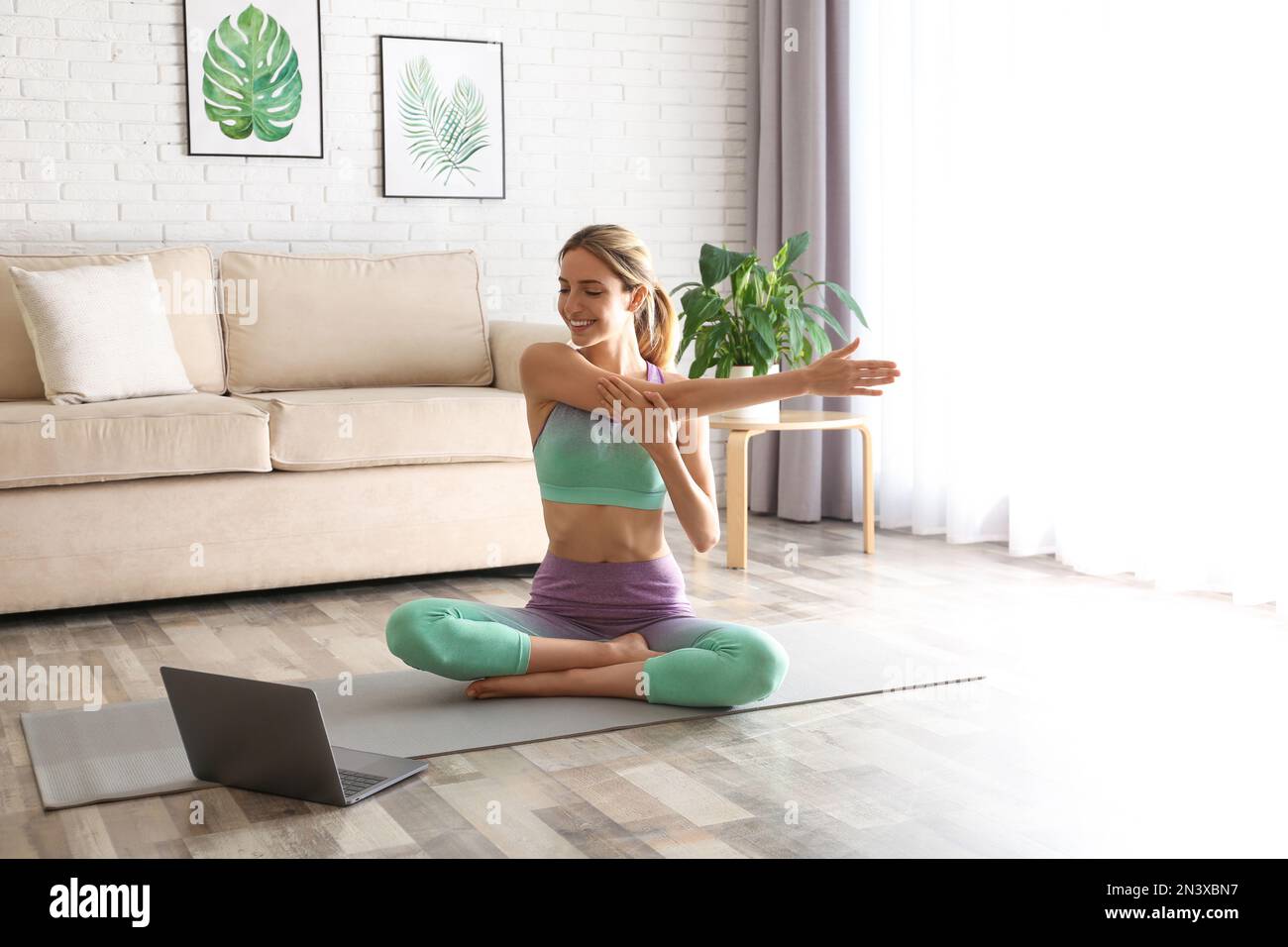 Frau, die zu Hause einen Online-Videokurs über ein Notebook führt. Distanz-Yoga-Kurs während der Coronavirus-Pandemie Stockfoto