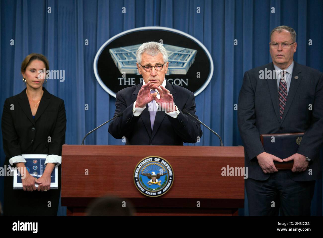 Defense Secretary Chuck Hagel, center, flanked by Deputy Defense Secretary Bob Work, right, and Principal Deputy Undersecretary of Defense for Personnel and Readiness Dr. Laura Junor, gestures during a news conference at the Pentagon, Wednesday, Oct. 1, 2014, to discuss the military health care system. (AP Photo/Cliff Owen) Stockfoto