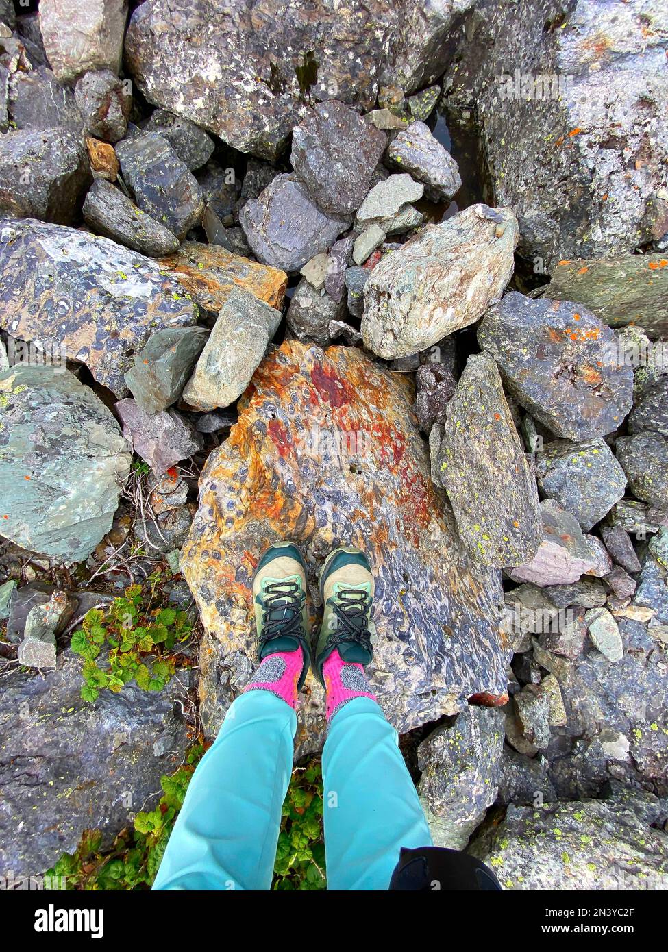 Blick nach unten auf die Beine und Wanderschuhe eines Mädchens, das auf hohen Bergsteinen steht. Stockfoto