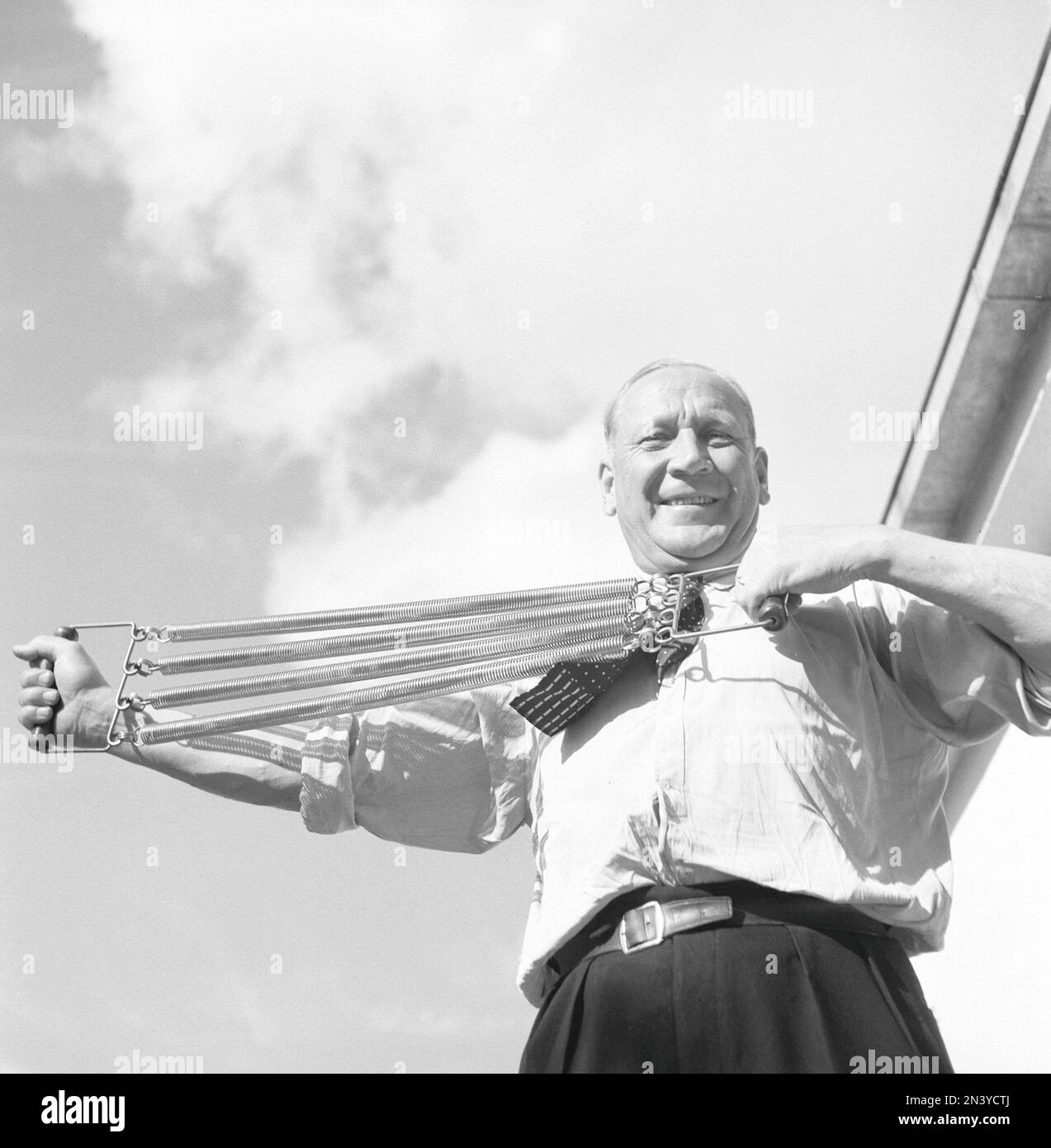 Starker Mann in den 1940er. Ein etwas älterer Mann zeigt, dass er keine Probleme hat, seine Armkraft zu benutzen und zu trainieren und mit einem Brustexpander zu trainieren. Schweden 1942 Kristoffersson Ref H5-5 Stockfoto