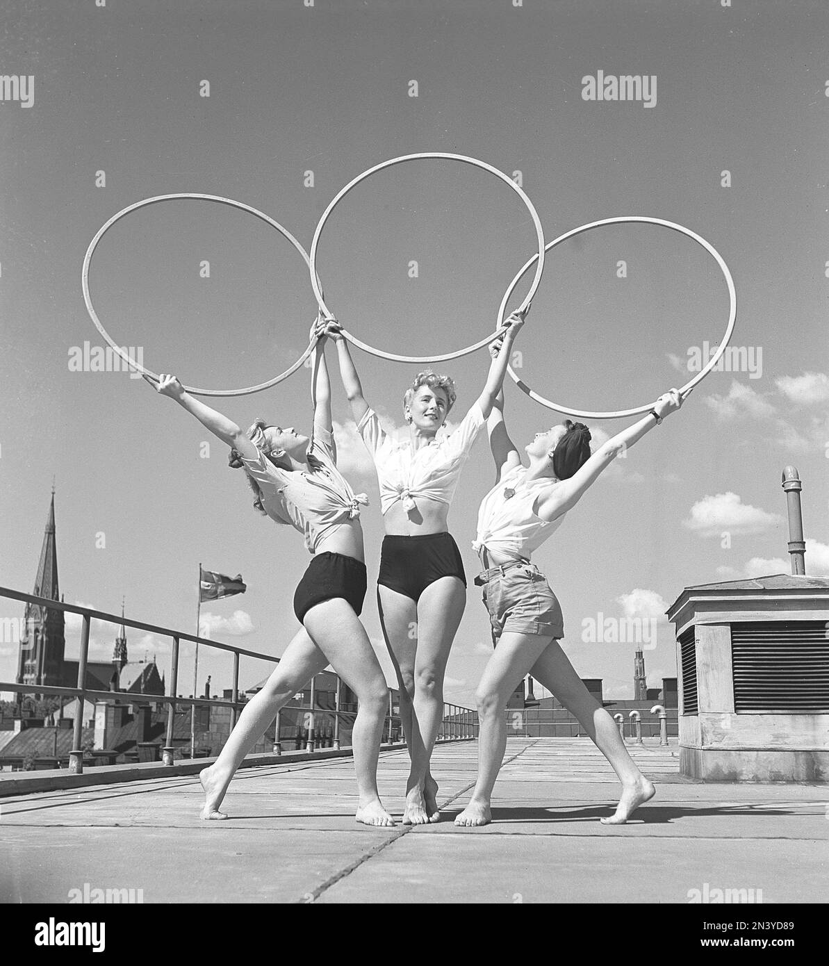 Gymnastik in den 1940er Jahren. Drei junge Turnerinnen stehen auf einem Dach in Stockholm und bilden ein symmetrisches Bild, wenn sie die drei Ringe über sich halten und posieren. Schweden 1945 Kristoffersson Ref O143-4 Stockfoto