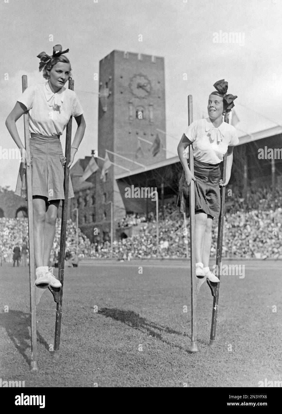 1950er Paar. Schauspielerin Sickan Carlsson rechts und ein Freund laufen und balancieren auf Stelzen auf dem Rasen des Stockholmer Stadions. Schweden 1939 Stockfoto