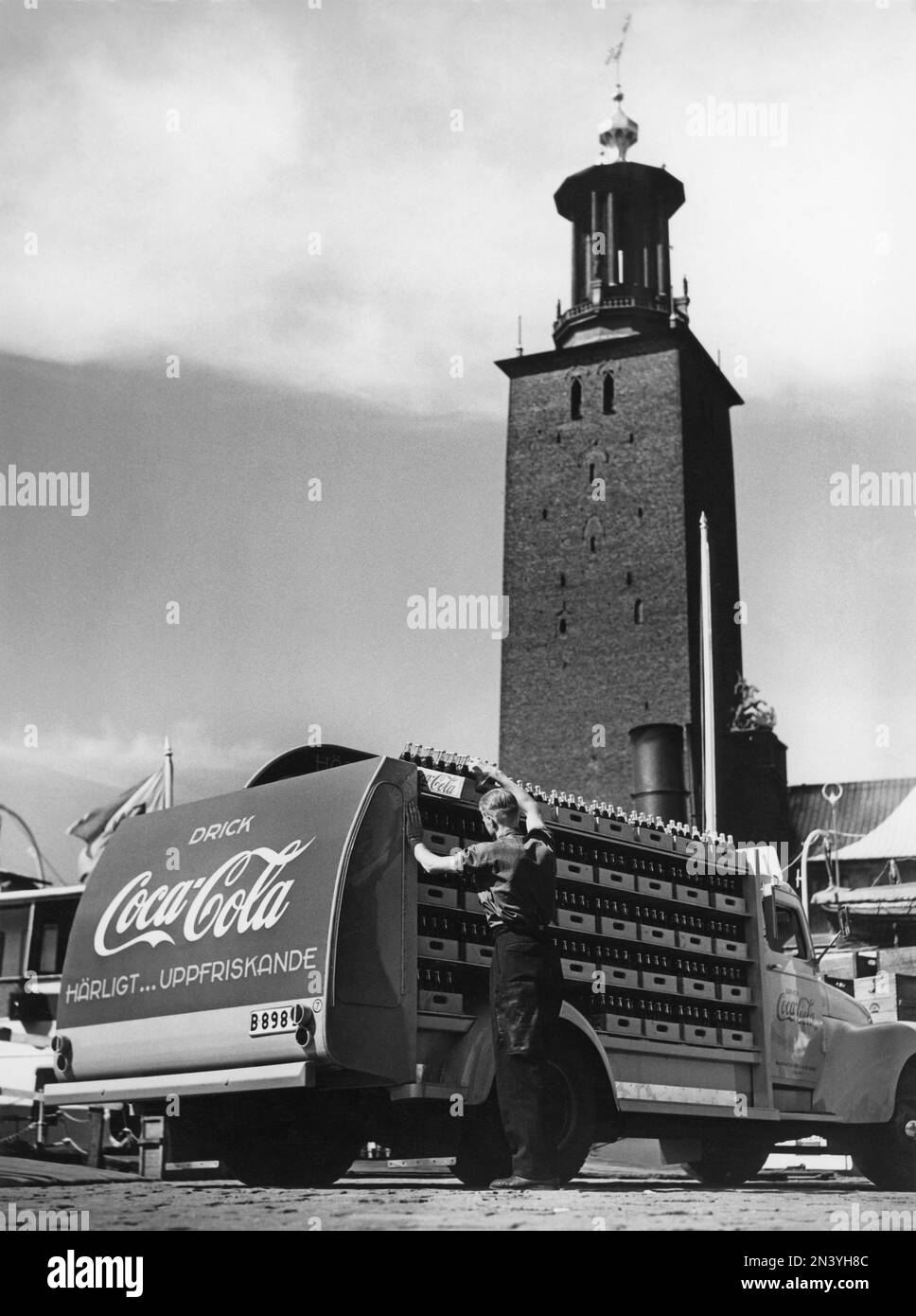 Coca Cola in den 1950er. Am 1. januar 1953 durfte Coca-Cola erstmals in Schweden hergestellt und verkauft werden; zuvor war der Verkauf in Schweden beschränkt, da der Coca-Cola-Gehalt verbotene Stoffe wie Phosphorsäure und Koffein enthielt. Einer der ersten Lieferwagen der Brauerei Mineralvattenfabriken Tre Kronor, beladen mit Coca-Cola-Flaschen, abgebildet in Stockholm mit dem Rathaus im Hintergrund. Volvo-Lkw, Modell L34, modifiziert und rot lackiert für den exklusiven Einsatz bei Coca-Cola-Lkw. Coca-Cola war früh dran mit Werbung für ihre Fahrzeuge. Schweden 1953 Stockfoto