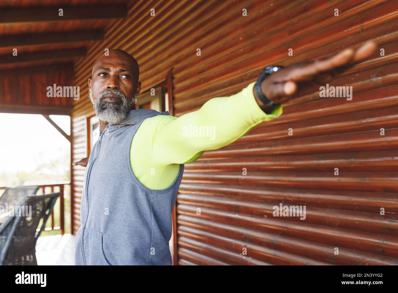Kahlköpfiger afroamerikanischer Seniorist mit ausgestreckten Armen, der gegen eine Holzwand in einer Blockhütte trainiert Stockfoto