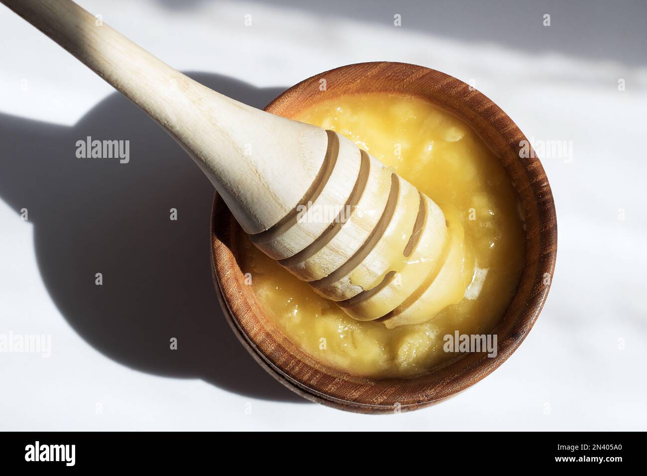 Honigstiel in einer Holzschüssel mit Honig in der Sonne. Gesunder Bio-dicker Honig Dippen aus einem Holzlöffel Honig, Nahaufnahme. Harter Schatten. Stockfoto