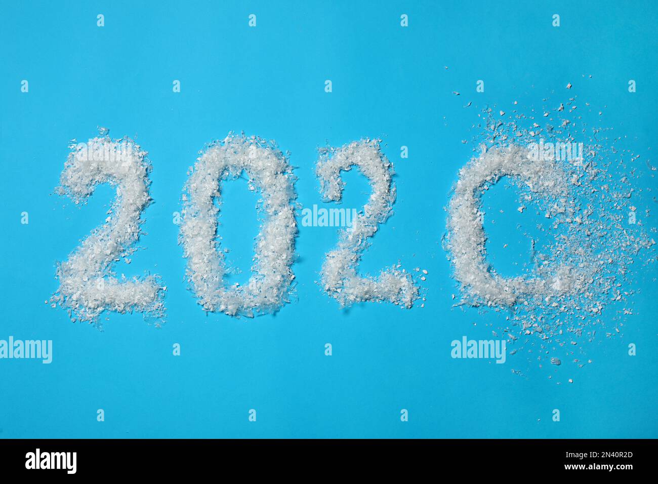 Das Jahr 2020 besteht aus künstlichem Schnee, der auf hellblauem Hintergrund weggeblasen wird, flach liegend Stockfoto