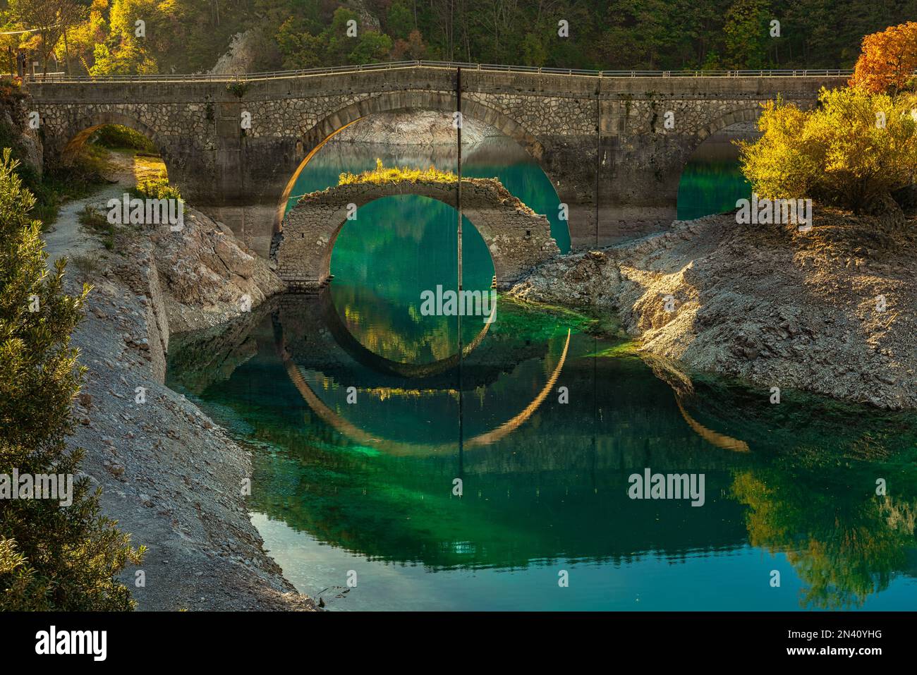 Die Herbstfarben der Bäume und zwei Brücken spiegeln sich im kristallklaren und türkisfarbenen Wasser der lak wider. Abruzzen, italien, Europa Stockfoto