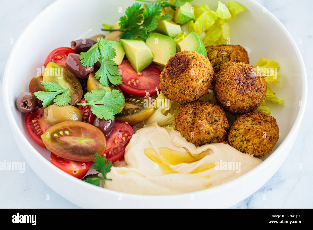 Falafel-Salatplatte mit Salat, Tomaten, Avocado, Hummus und Oliven. Gesundes veganisches Essen, israelische Küche. Stockfoto