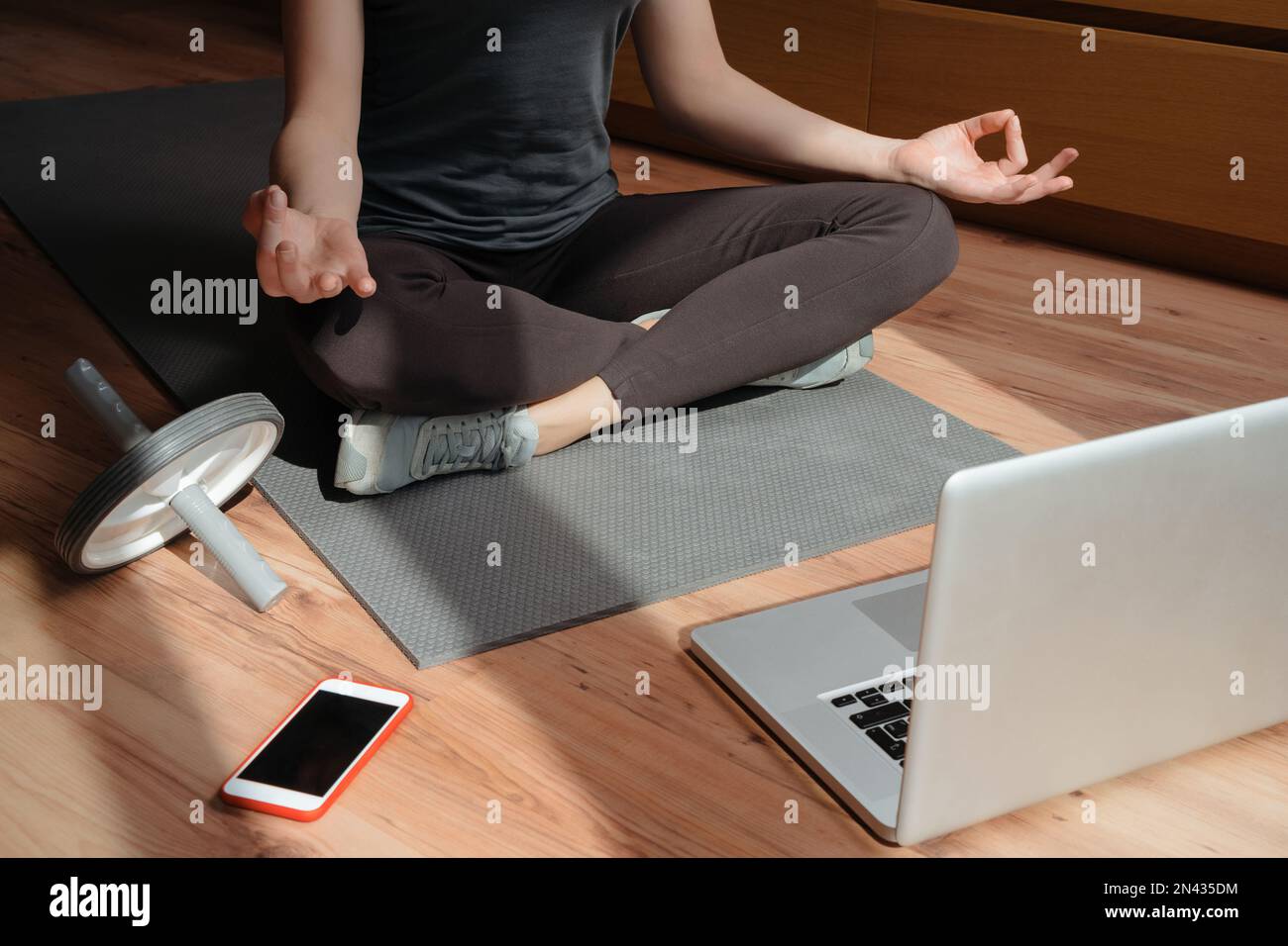 Junge sportliche Frau, die zu Hause auf dem Boden mit Laptop und Smartphone Yoga praktiziert und dabei Ruhe und Sicherheit einflößt. Video-Onlineschulung, Sukhasana-Haltung, entspannt atmen. Konzept eines gesunden Lebensstils Stockfoto