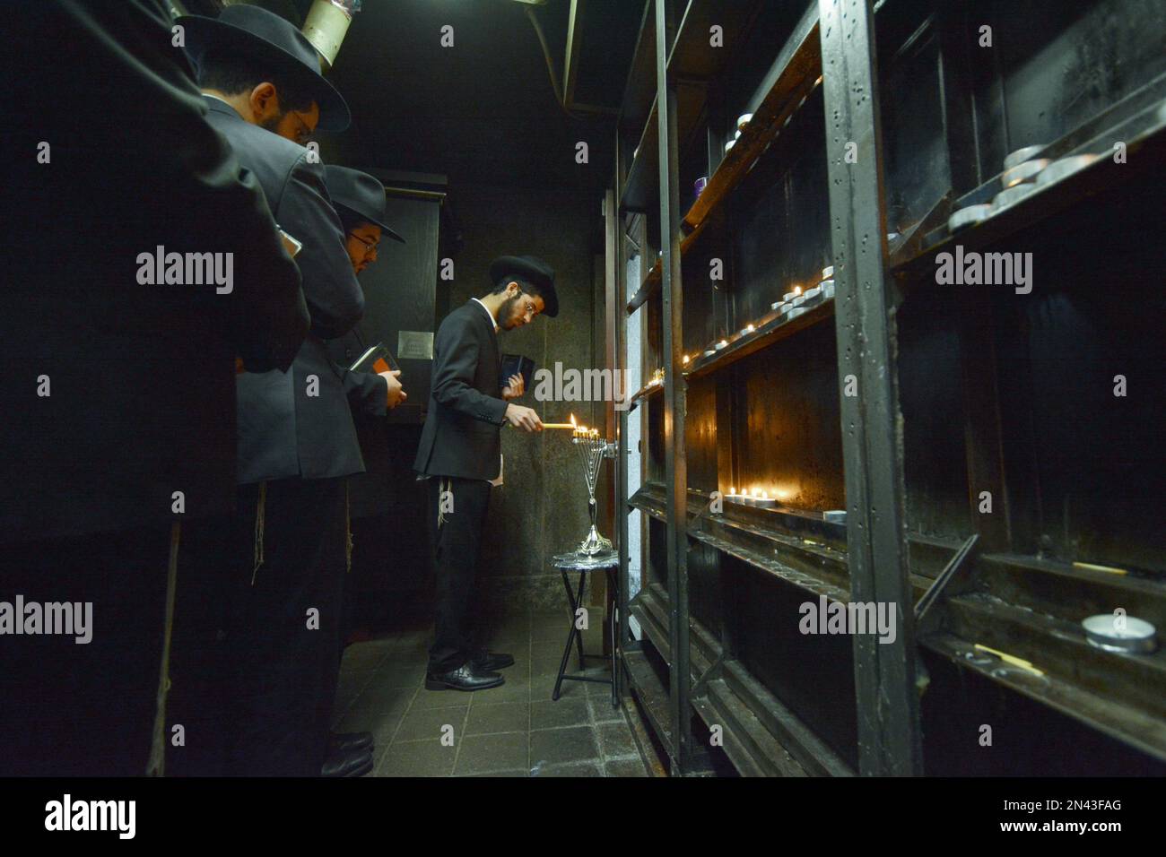 Junge Männer aus Chabad zünden eine Chanukkah Menorah in einem kleinen Raum im Ohel an, neben den Grabsteinen der letzten 2 Lubavitcher Rebbes. In Queens, New York City. Stockfoto