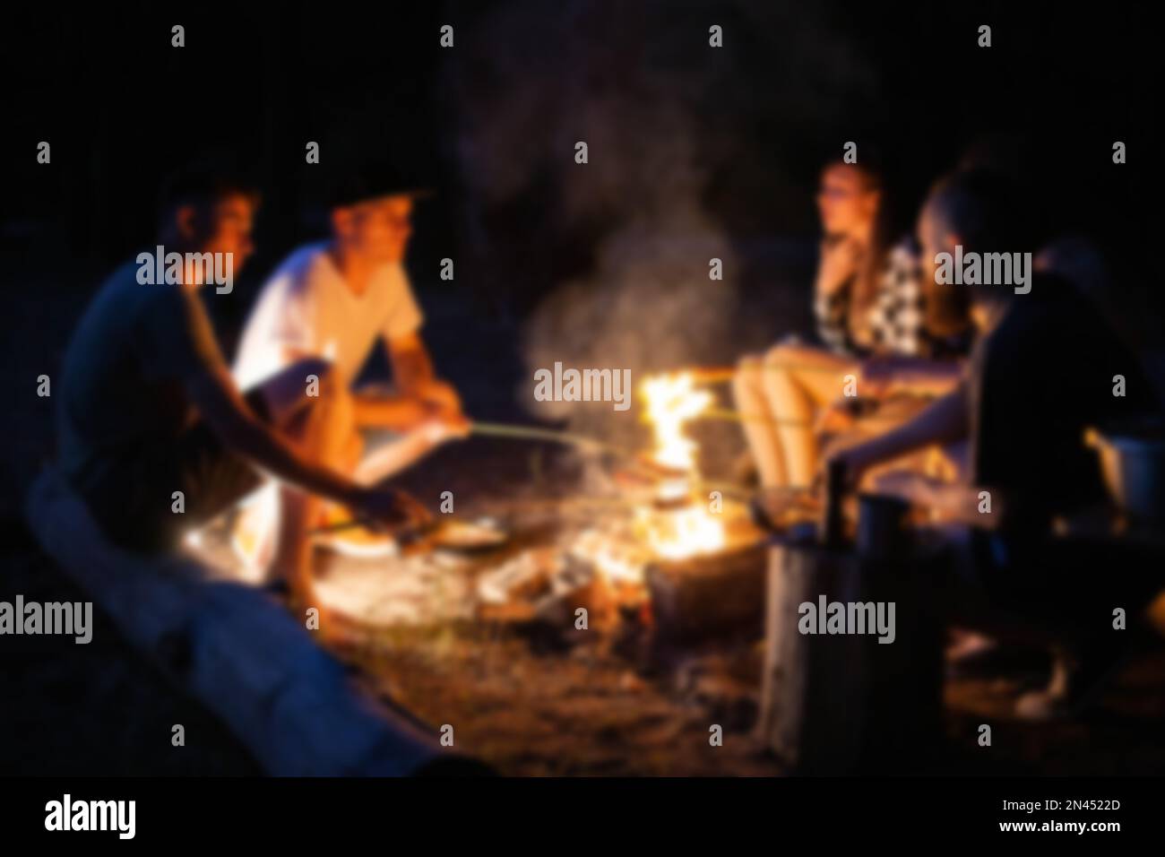 Junge Menschen ruhen sich nachts in der Natur aus. Kochen in der Nähe des Feuers auf dem Hintergrund von Schals, verschwommen. Platz für Text kopieren Stockfoto