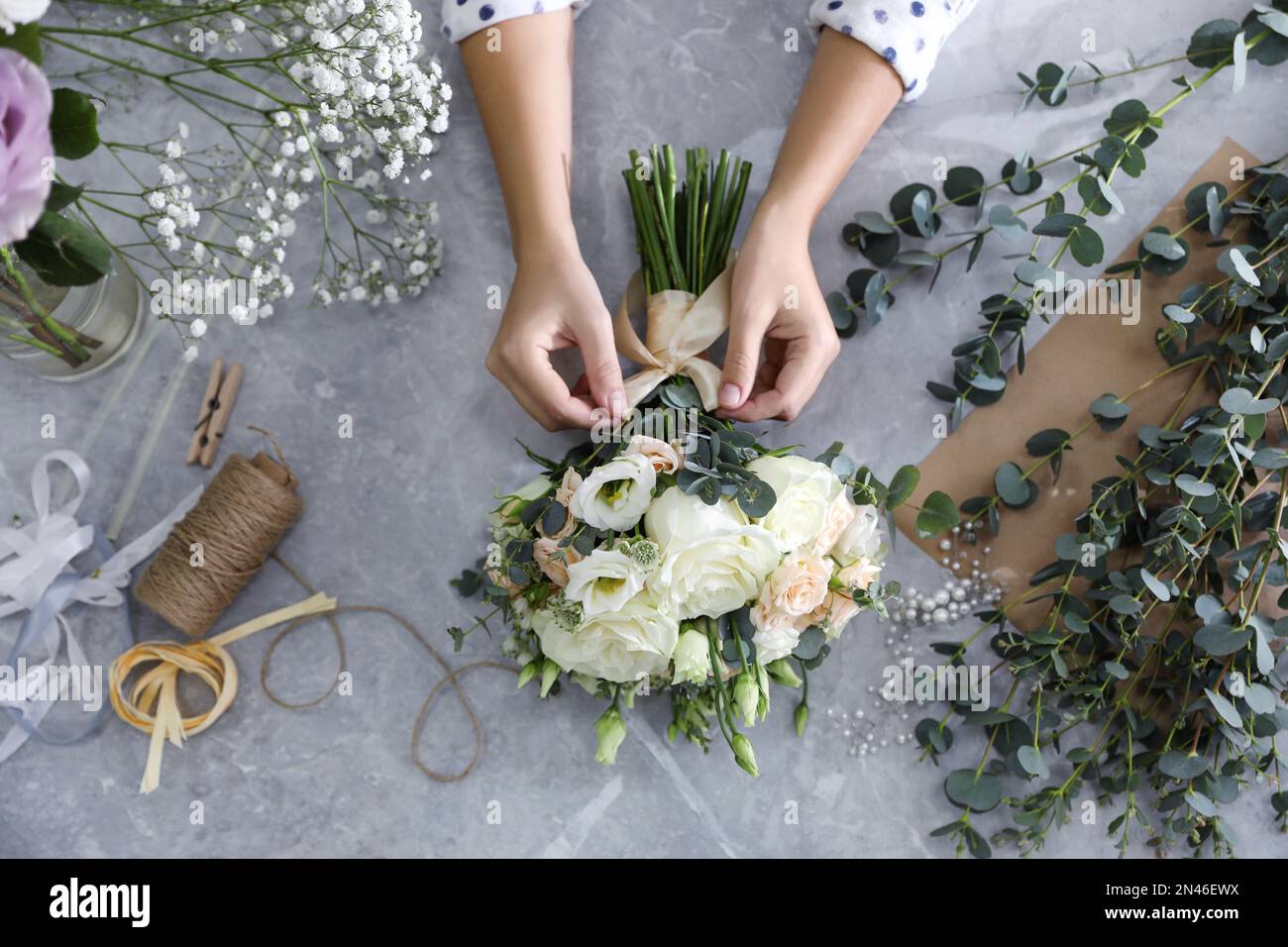 Florist auf wunderschönem Hochzeitsstrauß am hellgrauen Marmortisch, Blick von oben Stockfoto