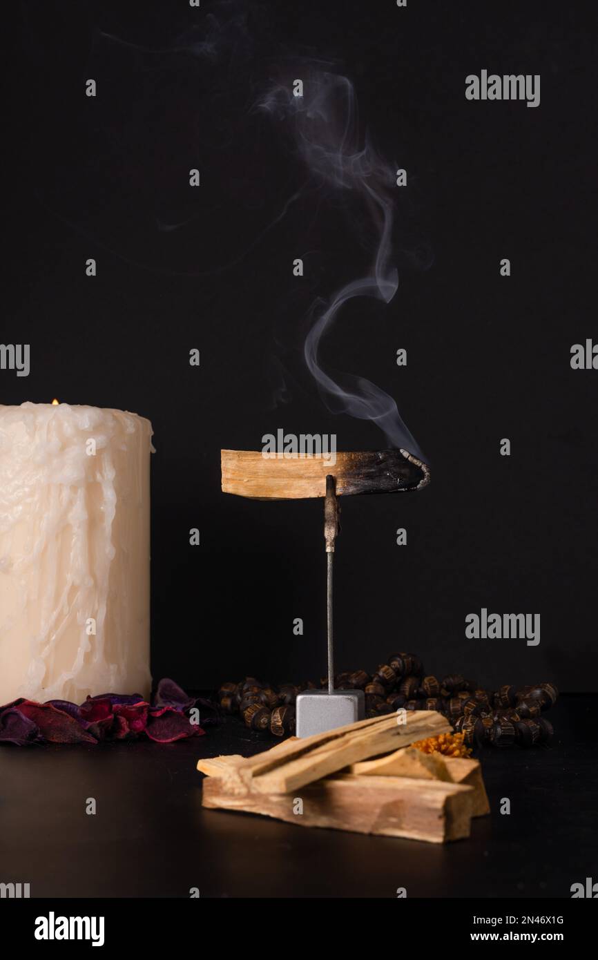 palo santo, heiliger Stock, raucht in einem Glasbecher mit brennenden Kerzen und dunklem Hintergrund Stockfoto