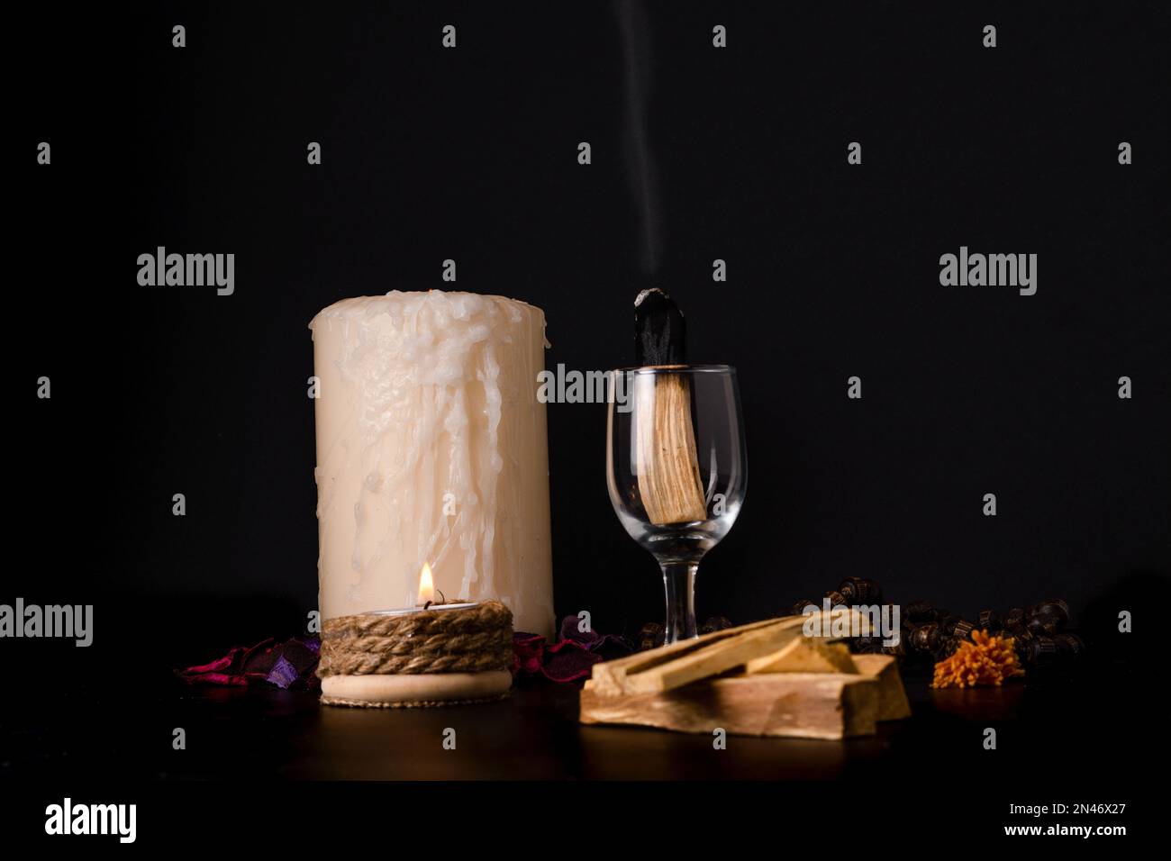 palo santo, heiliger Stock, raucht in einem Glasbecher mit brennenden Kerzen und dunklem Hintergrund Stockfoto