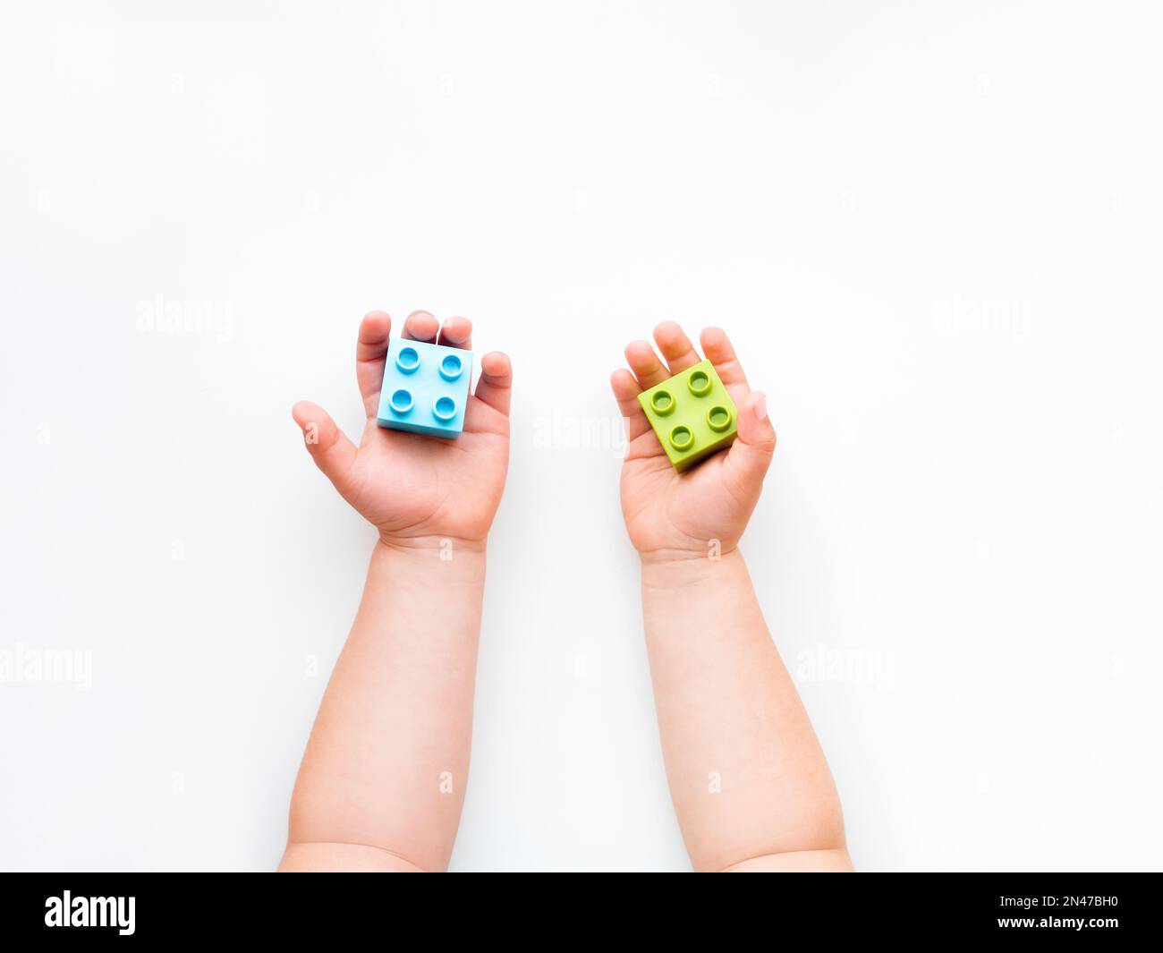 Das Kind spielt mit bunten Bausteinen. Kinderhände mit Ziegelspielzeug auf weißem Hintergrund. Pädagogisches Spielzeug, flach liegend, Draufsicht. Stockfoto