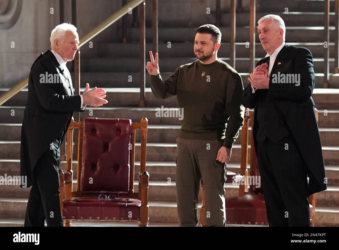 Der ukrainische Präsident Volodymyr Zelensky gibt ein Friedenszeichen, da er vom Präsidenten des Unterhauses, Sir Lindsay Hoyle (rechts), Lord McFall (links), Sprecher des Oberhauses, nach seiner Rede vor Parlamentariern in Westminster Hall, London, während seines ersten Besuchs im Vereinigten Königreich seit der russischen Invasion in der Ukraine. Stockfoto