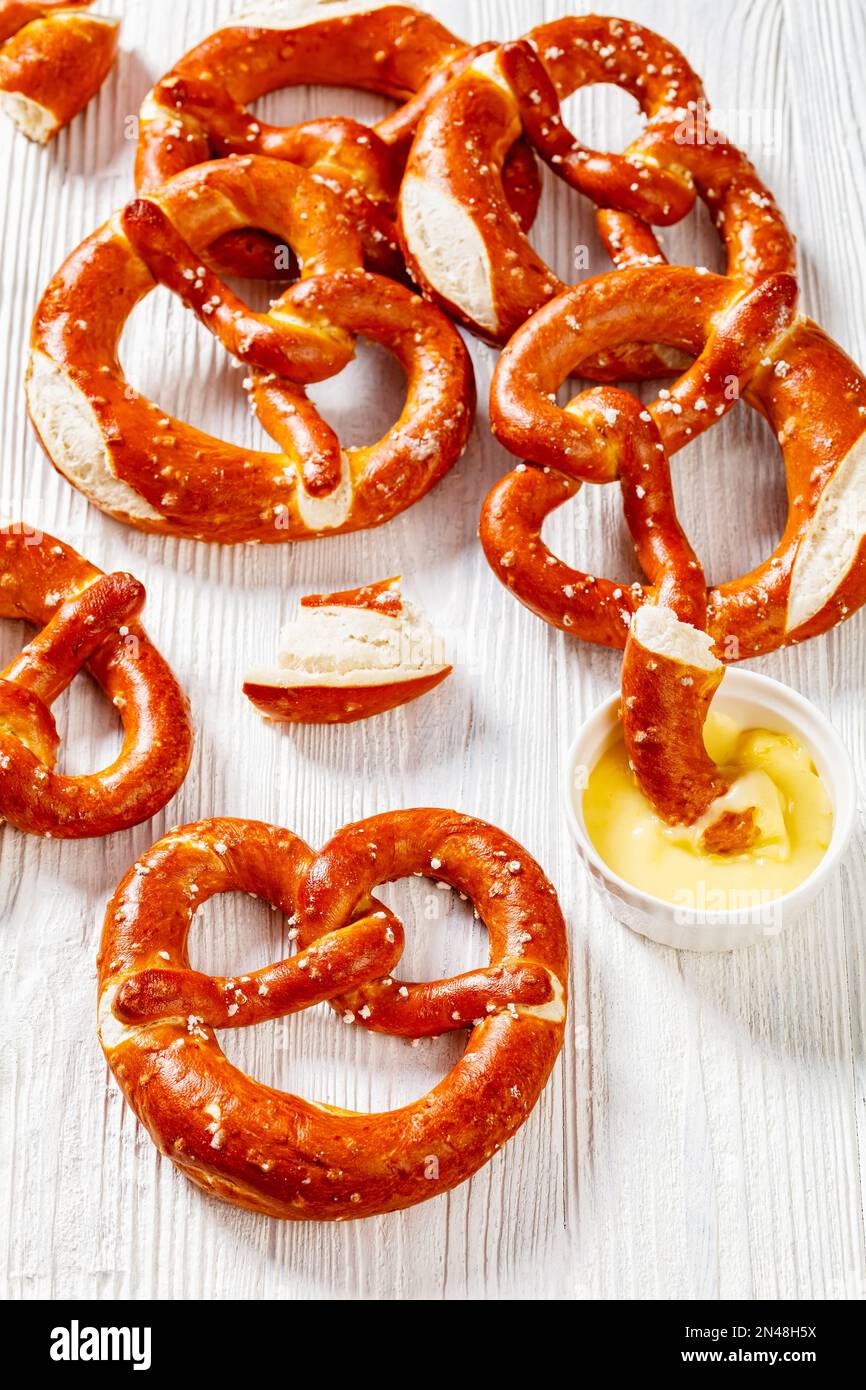 Weiche Brezeln in Form von Knoten gebacken und mit Salz auf weißem Holztisch mit Käsesauce bestreut, vertikale Ansicht von oben, Nahaufnahme Stockfoto