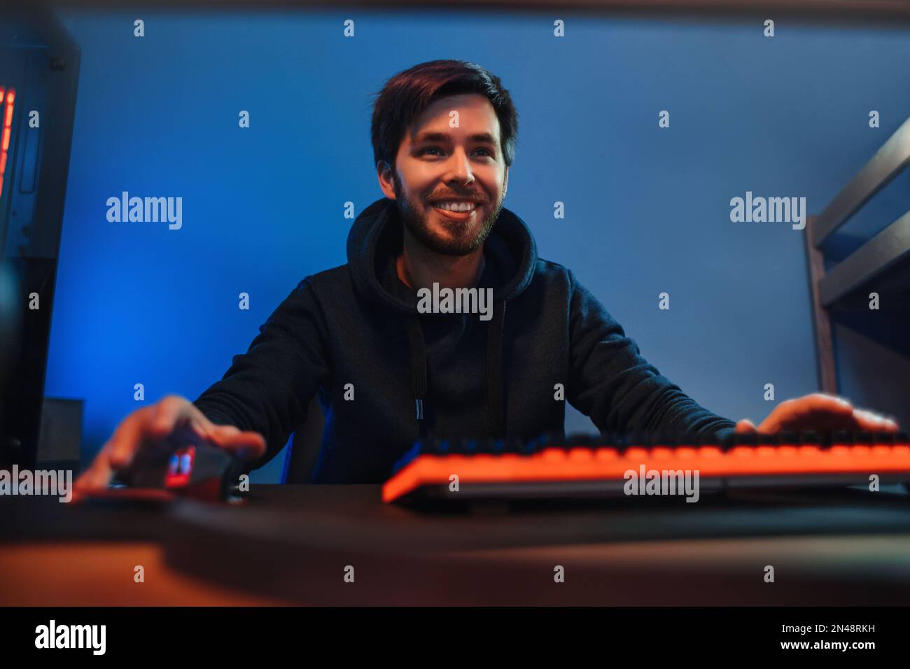 Porträt eines jungen Pro-Gamer, der Spaß hat, abends Online-Videospiele zu Hause spielt, Videospiele streamt. Guy spielt Multiplayer-Spiel mit Freunden. Vorderansicht, Hintergrund, Neonfarbe Stockfoto