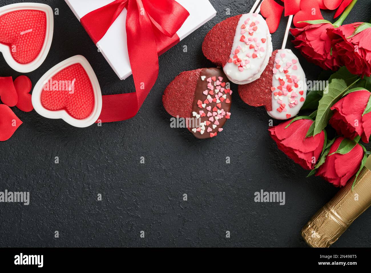 Valentinskarte. Rosa Blumen Brownie Kekse und Schokoladenbonbons in Herzform, Geschenkbox mit Wein auf schwarzem Hintergrund. Mütter oder Frauen D. Stockfoto