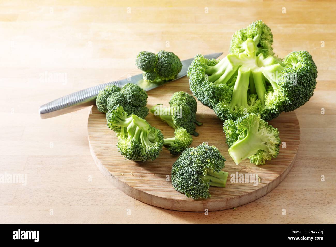 Roher Brokkoli und ein Küchenmesser auf einem Holzschneidbrett, gesundes Gemüse, Vorbereitung zum Kochen einer vegetarischen Mahlzeit, Kopierraum, auswählen Stockfoto