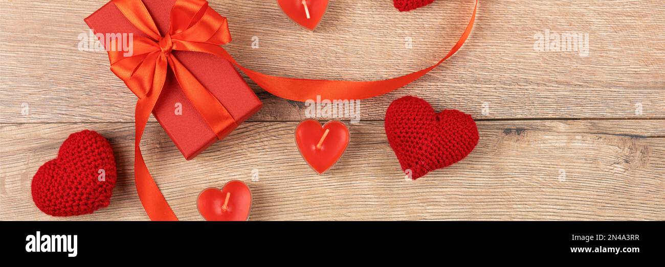 Rote Geschenkbox mit gestrickten roten Herzen und mit roten Kerzen in Herzform auf Holzhintergrund. Alles gute zum Valentinstag, Muttertag und bir Stockfoto