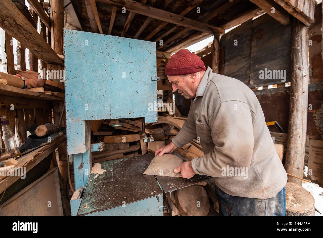 Ein älterer Mann, der Holz auf einer Maschine in einer Außenwerkstatt verarbeitet. Stockfoto