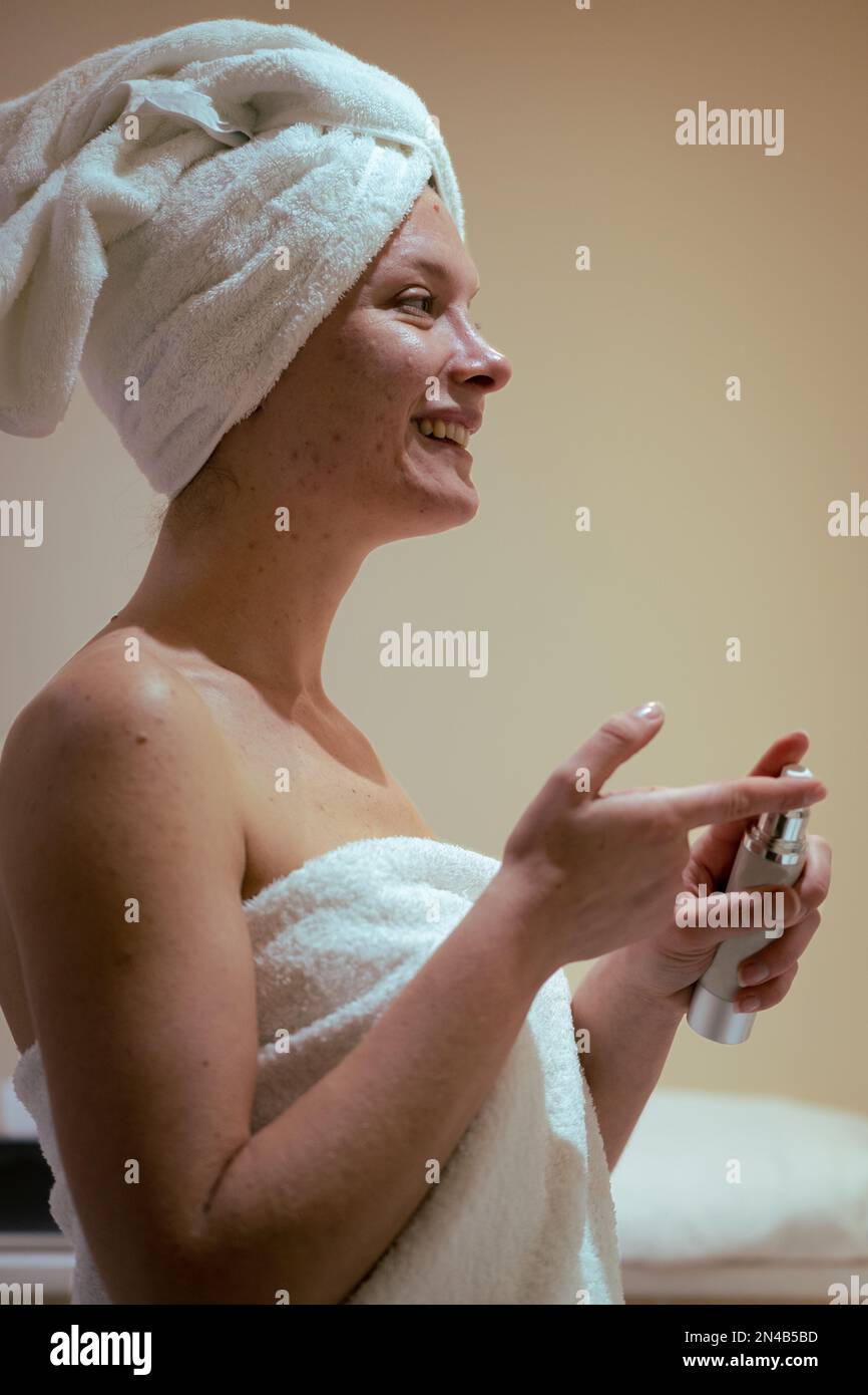 Vertikale lächelnde Frau, die Anti-Akne Creme im Gesicht aufträgt, im Badezimmer, Hautpflege-Routine Stockfoto