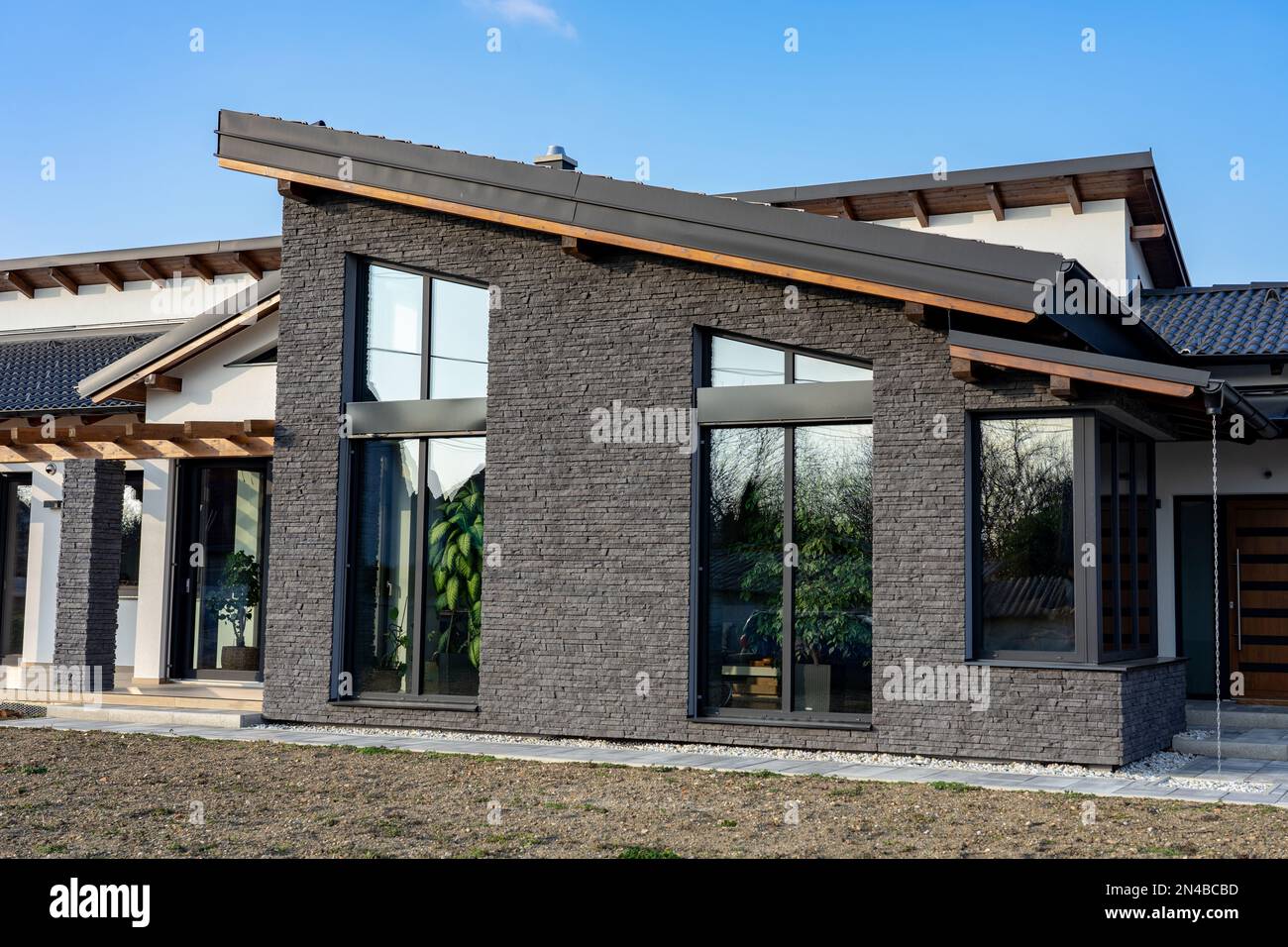 Modernes Haus mit Naturatmosphäre, hölzernen Felsdetails und Pflanzen und großen Fenstern Stockfoto
