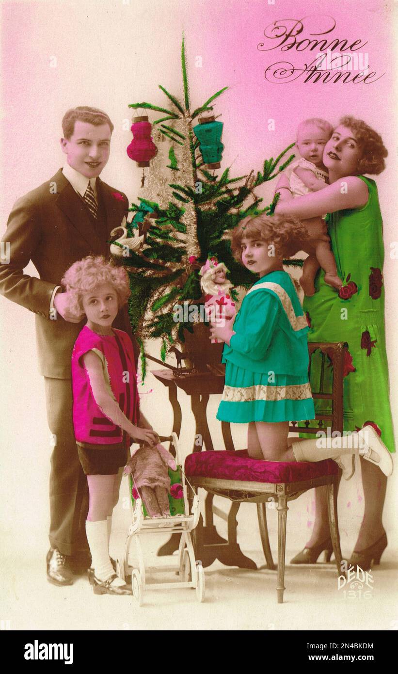 Edwardianische Ära Belle Epoque Französische Neujahrsgrüße Postkarte mit einer jungen Familie um einen Weihnachtsbaum herum. Ungefähr 1910 Stockfoto