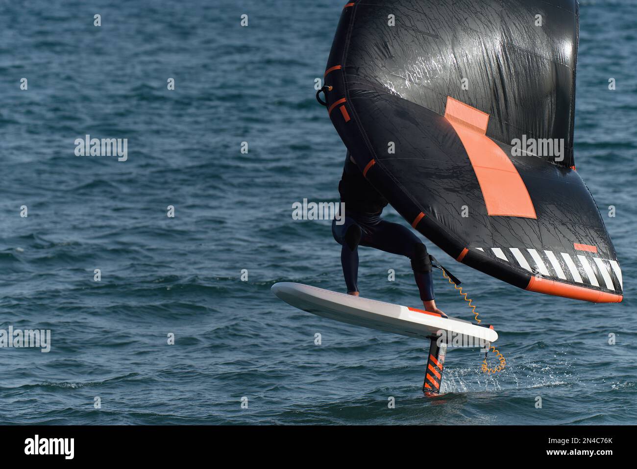 Ein Mann trägt Flügelfolien mit handgeführten aufblasbaren Flügeln und Tragflächensurfbrettern in einem blauen Ozean, reitet auf einem Windflügelbrett, surft auf den Wellen Stockfoto