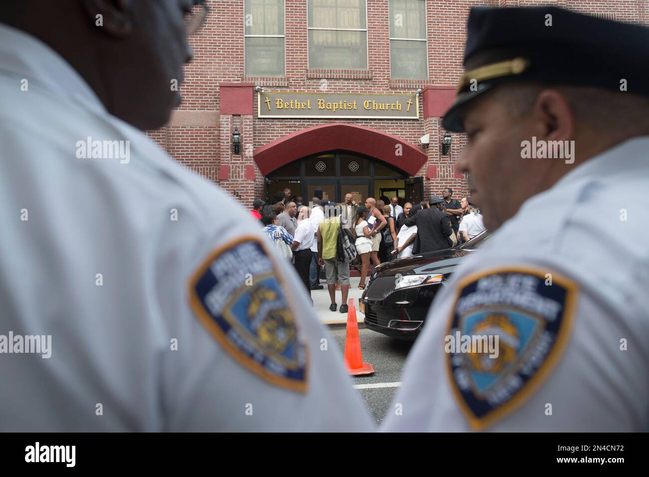 Mourners arrive as NYPD officers stand guard at the funeral service of Eric Garner, the 43-year-old New York City man whose death while in police custody has led to accusations of police misconduct, at Bethel Baptist Church, Wednesday, July 23, 2014, in the Brooklyn borough of New York. (AP Photo/John Minchillo) Stockfoto