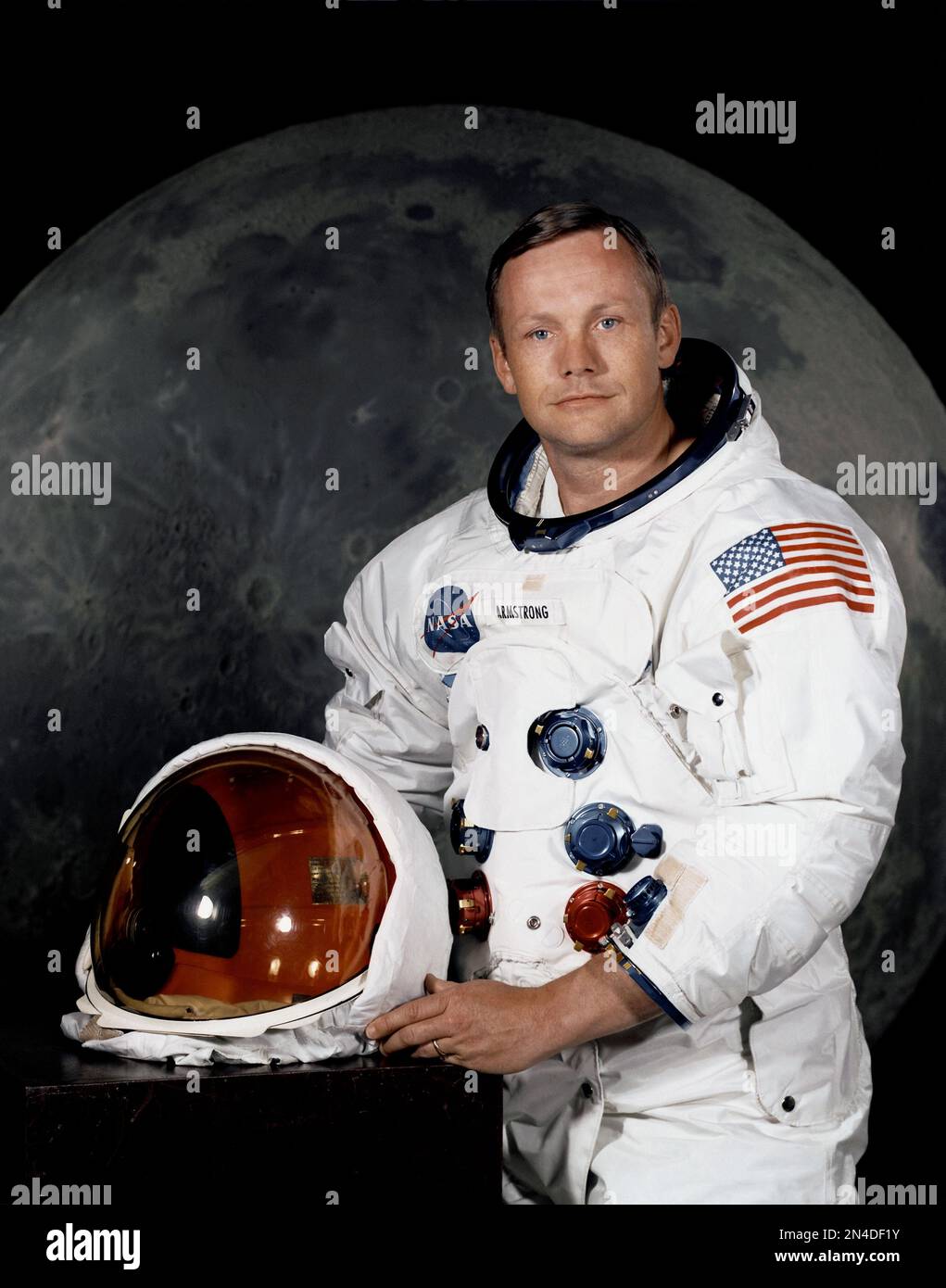 Portrait von Astronaut Neil A. Armstrong, Befehlshaber der Apollo 11 Lunar Landing Mission in seinem Raumanzug, mit seinem Helm auf dem Tisch vor ihm. Hinter ihm ist ein großes Foto der Mondoberfläche. Stockfoto