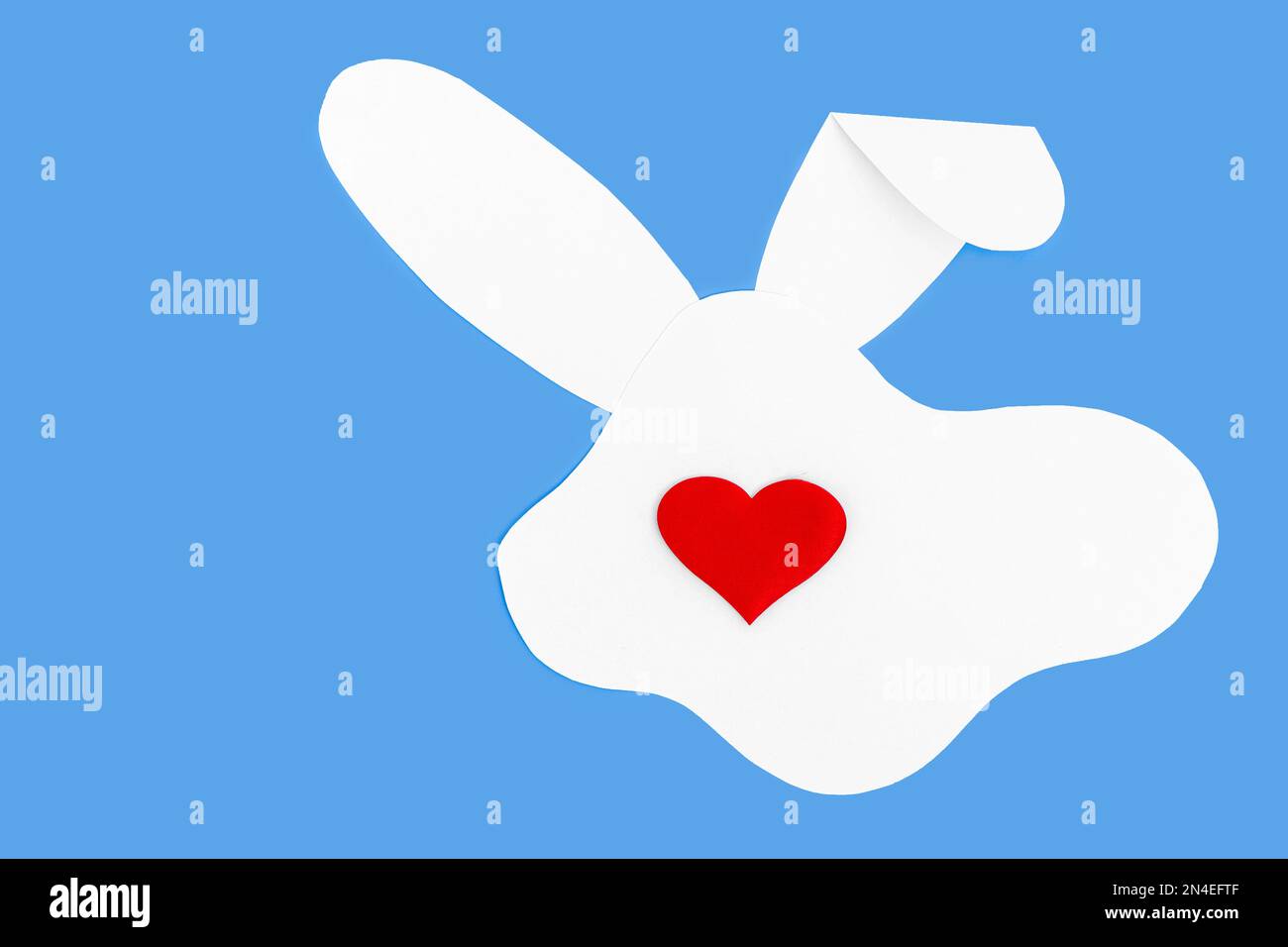 Kreatives Layout mit einer Silhouette aus weißem Papierhasen und einem roten Herz anstelle einer Nase auf blauem Hintergrund. Minimales Frühlingsferienkonzept. Stockfoto