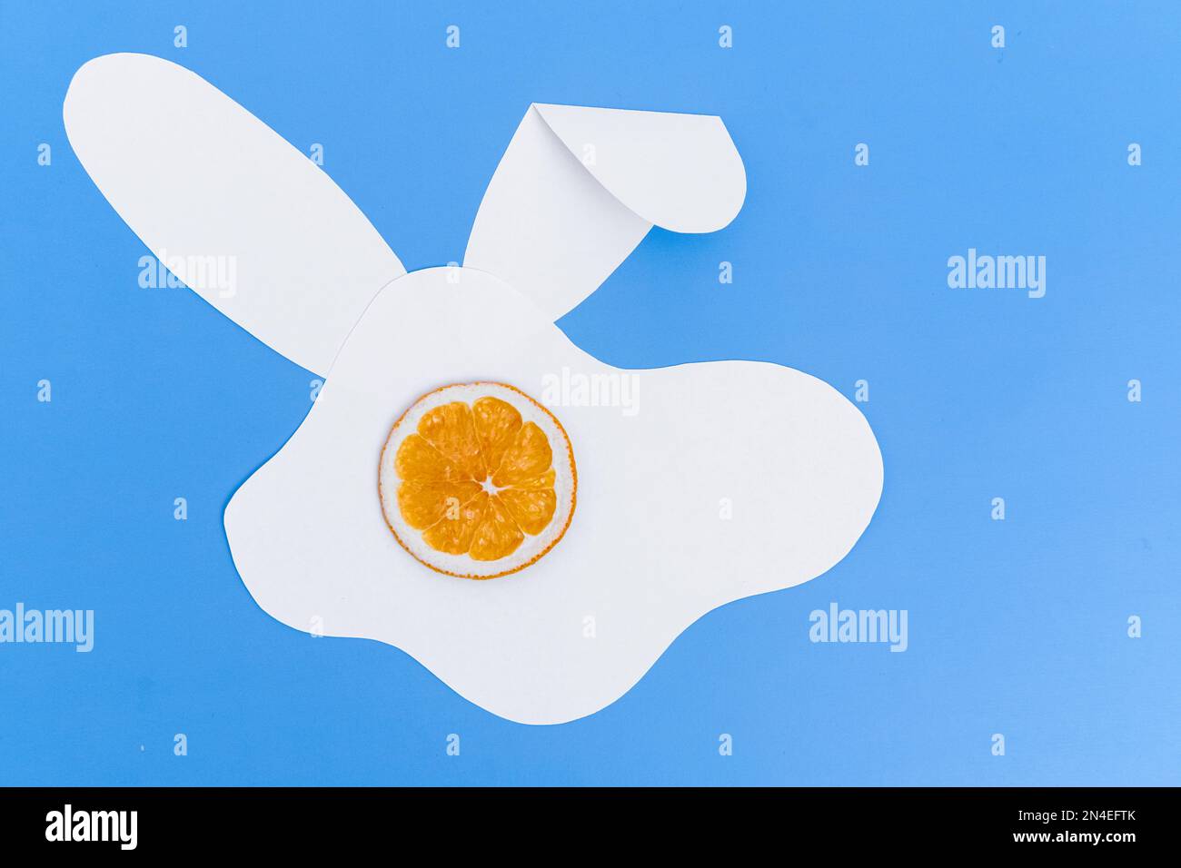 Kreatives Layout aus einer Silhouette eines weißen Papierkaninchens und einer Tasse getrockneter Orange auf blauem Hintergrund. Minimales Frühlingsferienkonzept. Stockfoto
