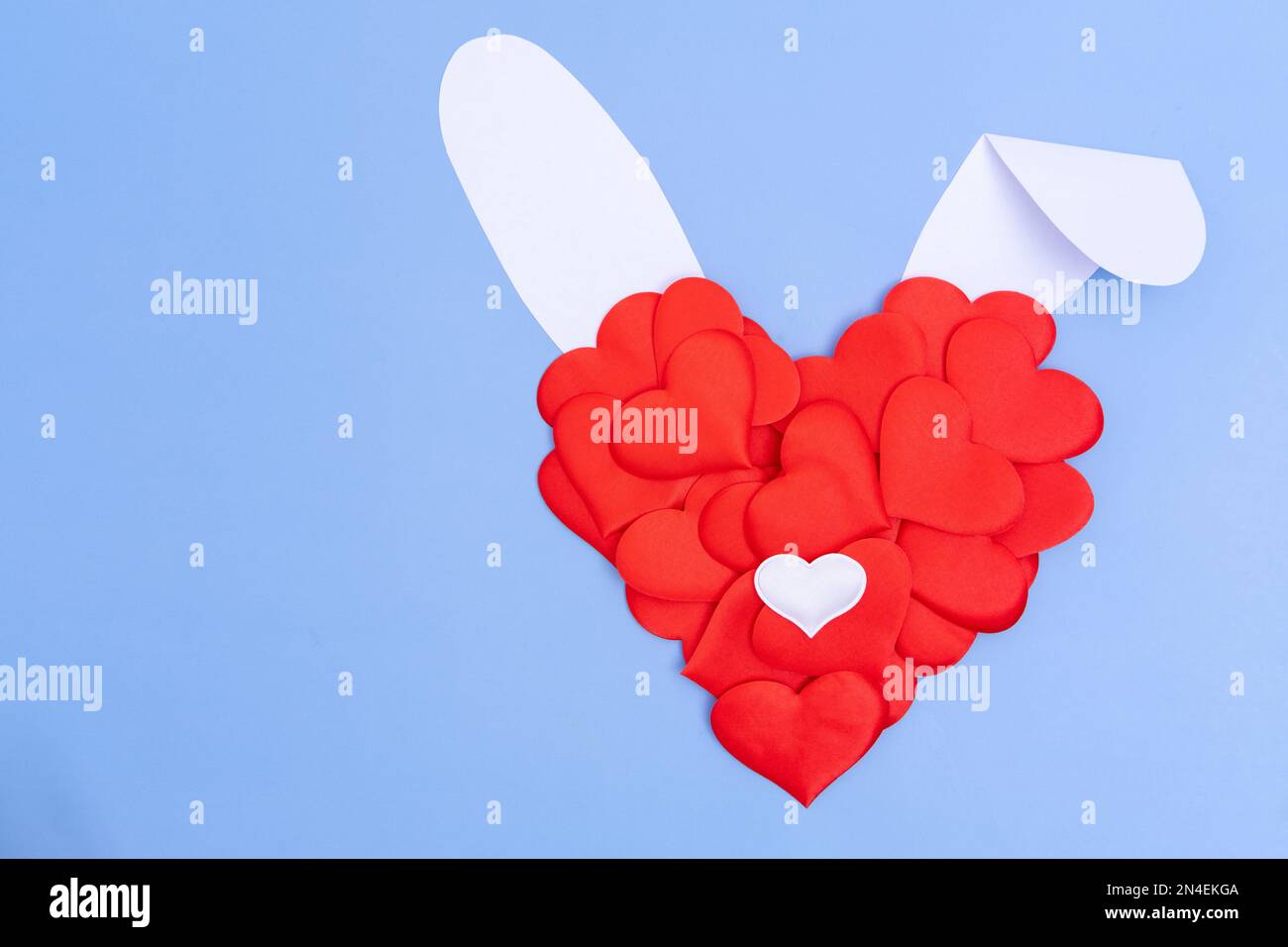 Kreative Grußkarte. Imitation des Osterhasen. Ein rotes Herz und weiße Papierohren auf blauem Hintergrund. Das Minimalkonzept eines Frühjahrsfeiertages. Stockfoto